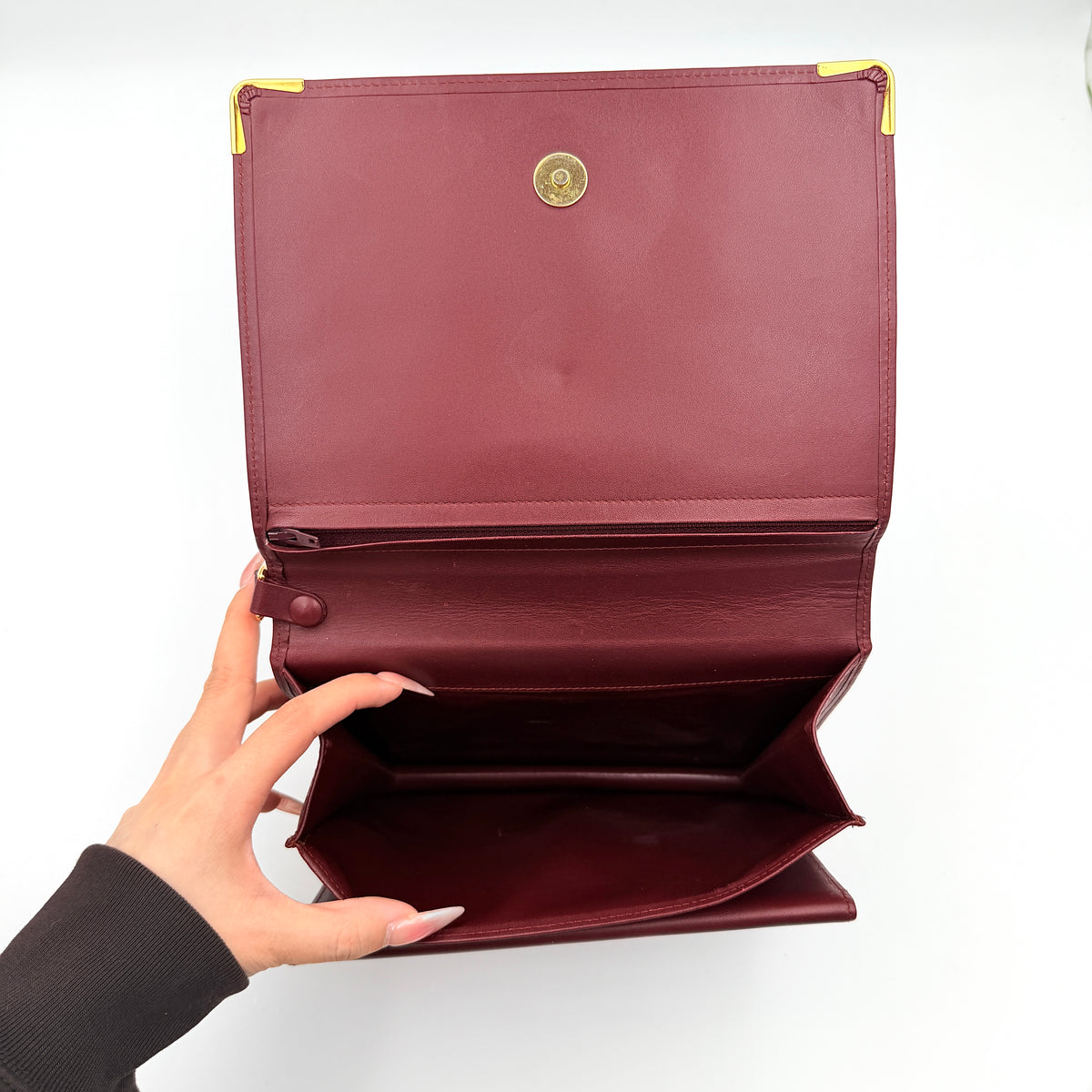 Cartier Must de Cartier wristlet clutch in burgundy leather with gold-tone corners and wrist strap, pictured with authenticity card and booklet.