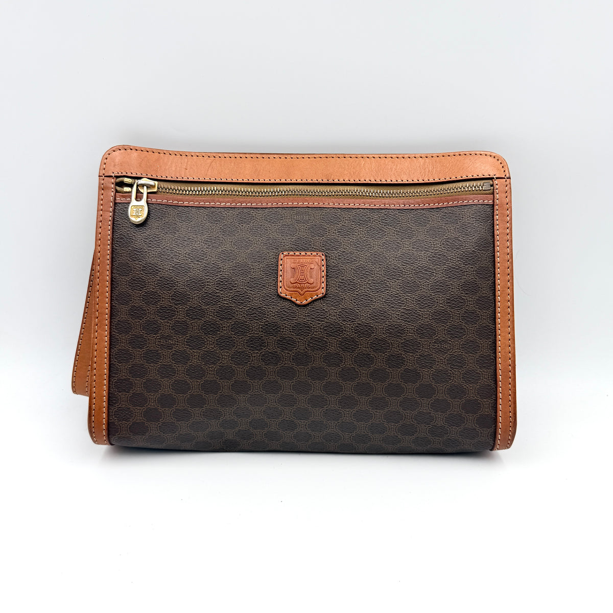 Celine Triomphe Macadam Clutch Bag in brown coated canvas with tan leather trim and gold zip, displayed against a white background.
