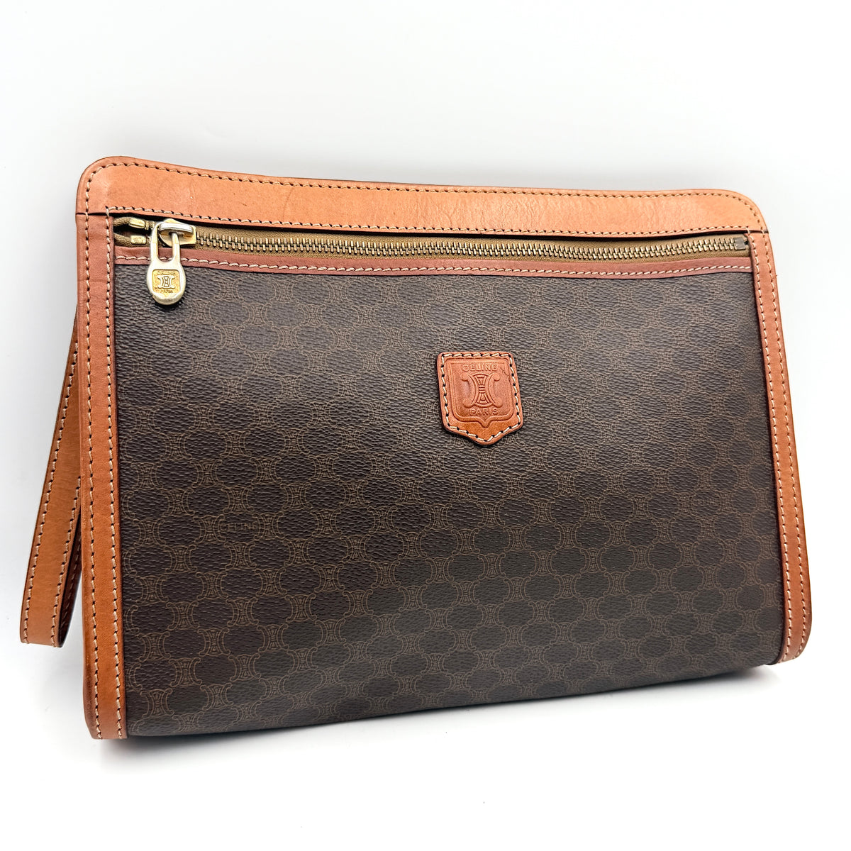Celine Triomphe Macadam Clutch Bag in brown coated canvas with tan leather trim and gold zip, displayed against a white background.