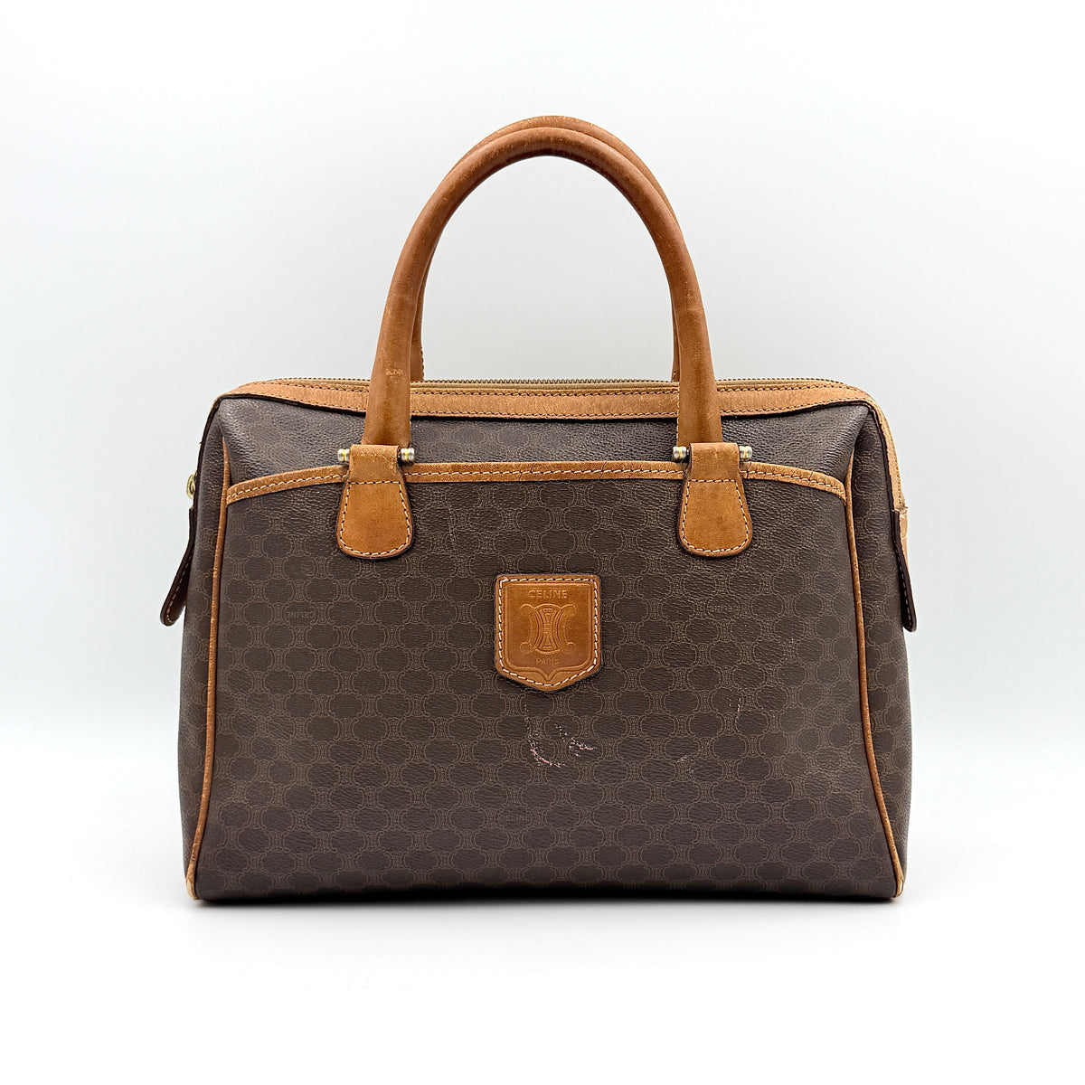 Celine Triomphe Macadam Boston Bag in brown coated canvas with tan leather trim and top handles, photographed against a white background.