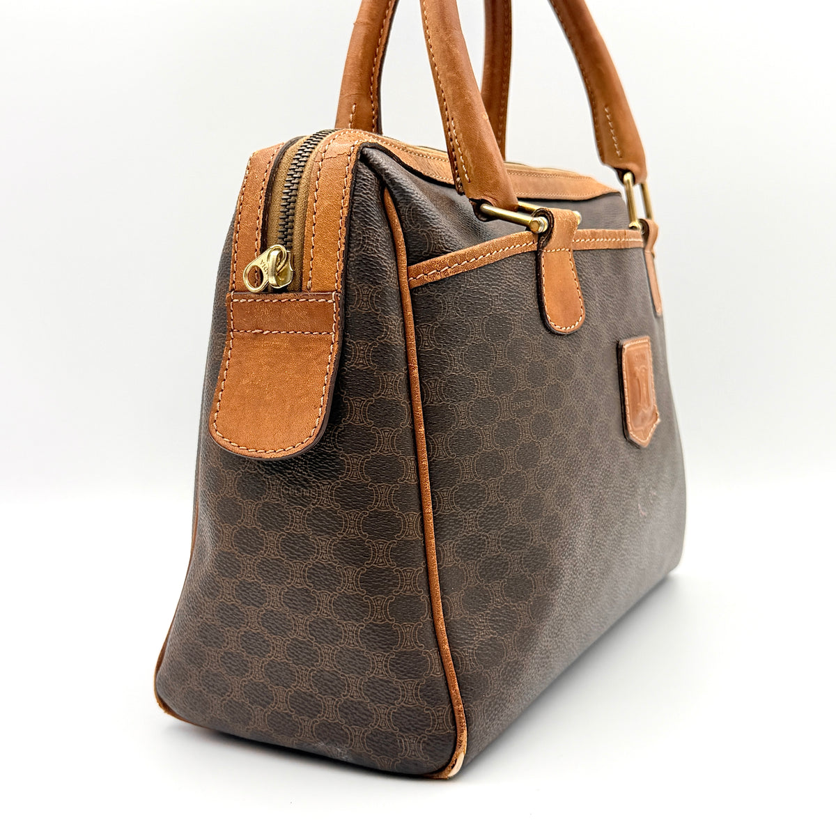 Celine Triomphe Macadam Boston Bag in brown coated canvas with tan leather trim and top handles, photographed against a white background.
