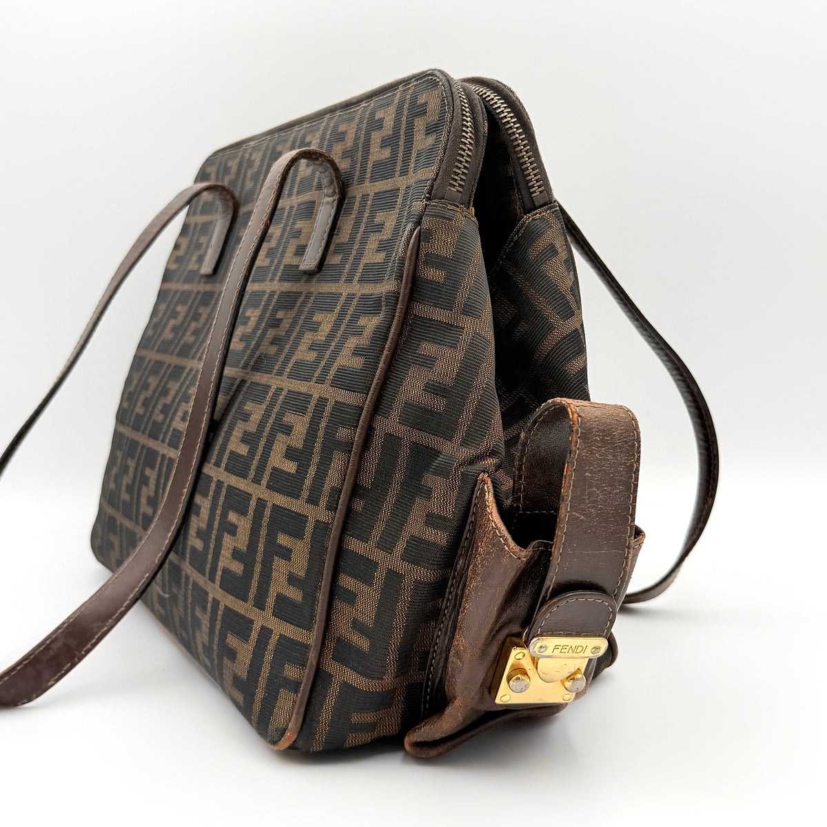 Fendi FF Zucca Double Zip Tote Bag in brown monogram canvas with leather straps and side pocket detail, shown on a yellow dust bag.