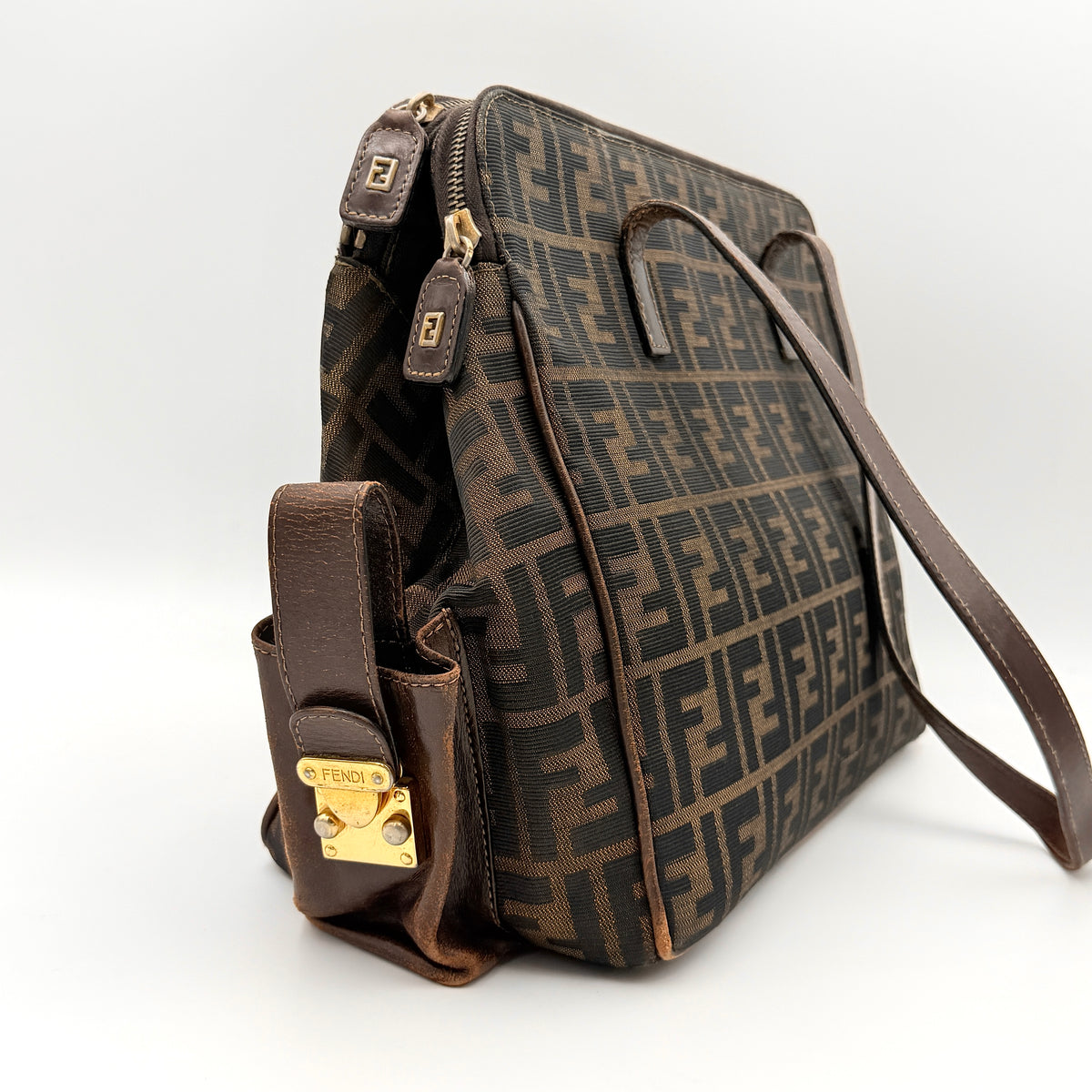 Fendi FF Zucca Double Zip Tote Bag in brown monogram canvas with leather straps and side pocket detail, shown on a yellow dust bag.