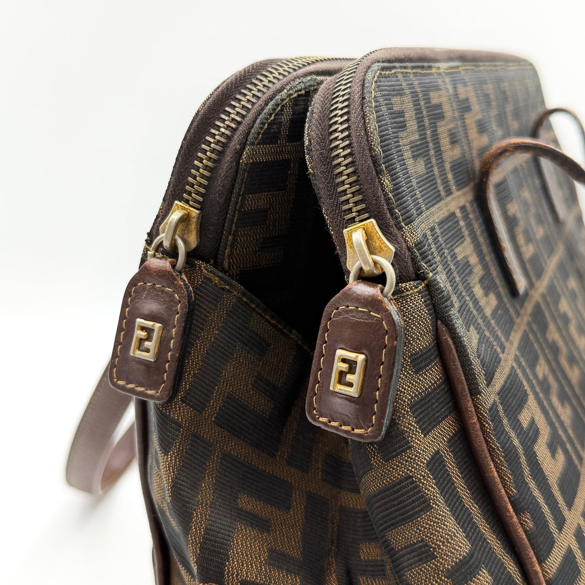 Fendi FF Zucca Double Zip Tote Bag in brown monogram canvas with leather straps and side pocket detail, shown on a yellow dust bag.