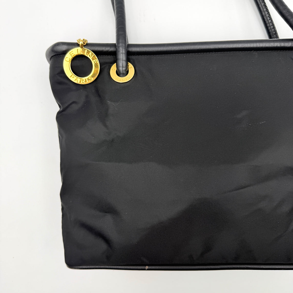 Black Celine nylon tote bag with gold circle logo hardware and leather handles, photographed flat on a white background.