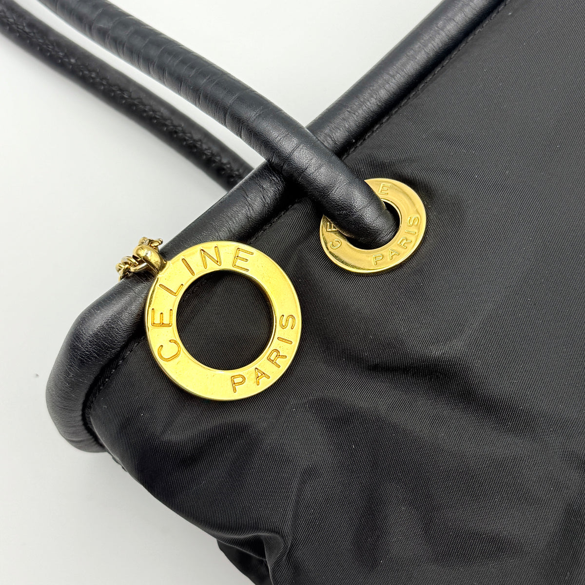 Black Celine nylon tote bag with gold circle logo hardware and leather handles, photographed flat on a white background.