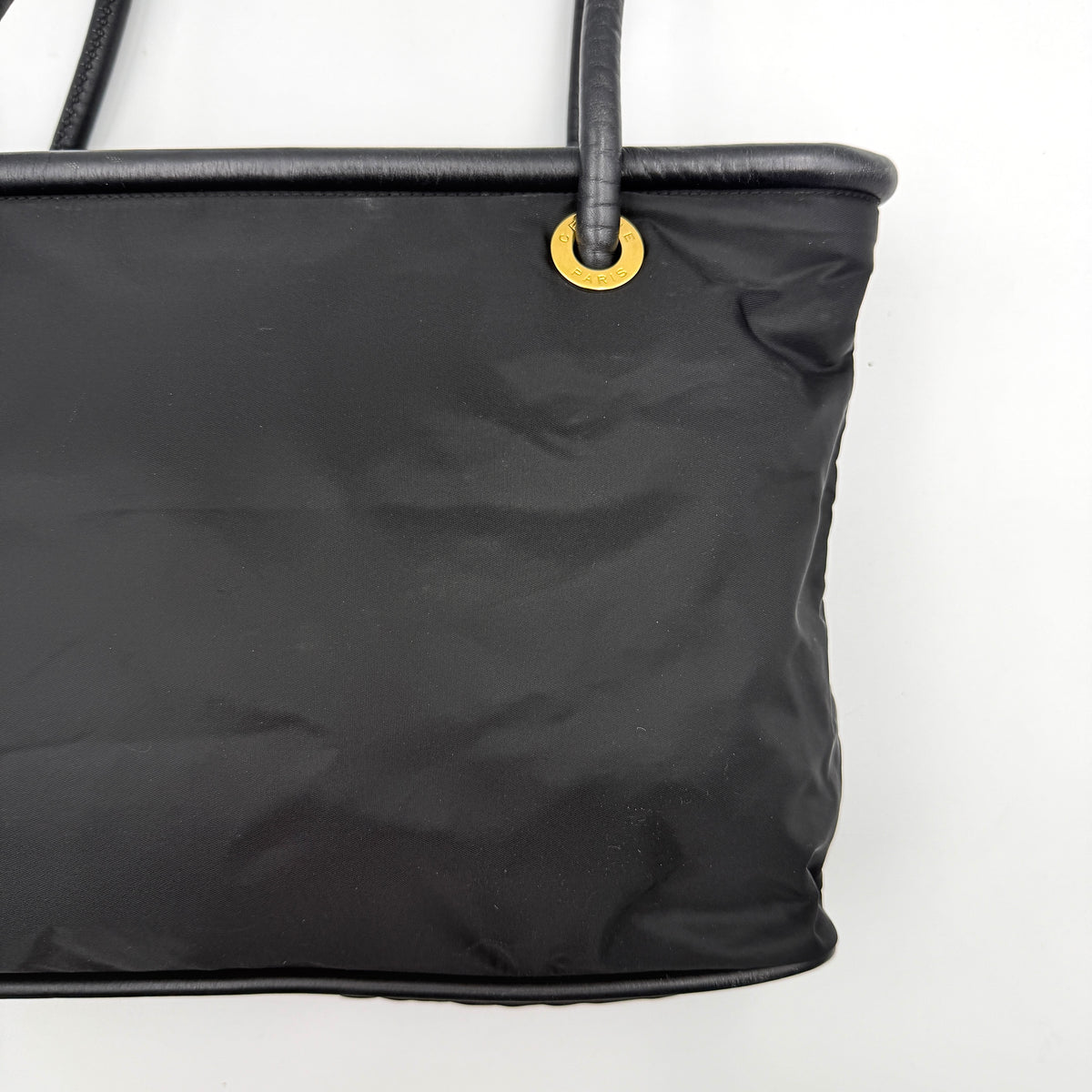 Black Celine nylon tote bag with gold circle logo hardware and leather handles, photographed flat on a white background.