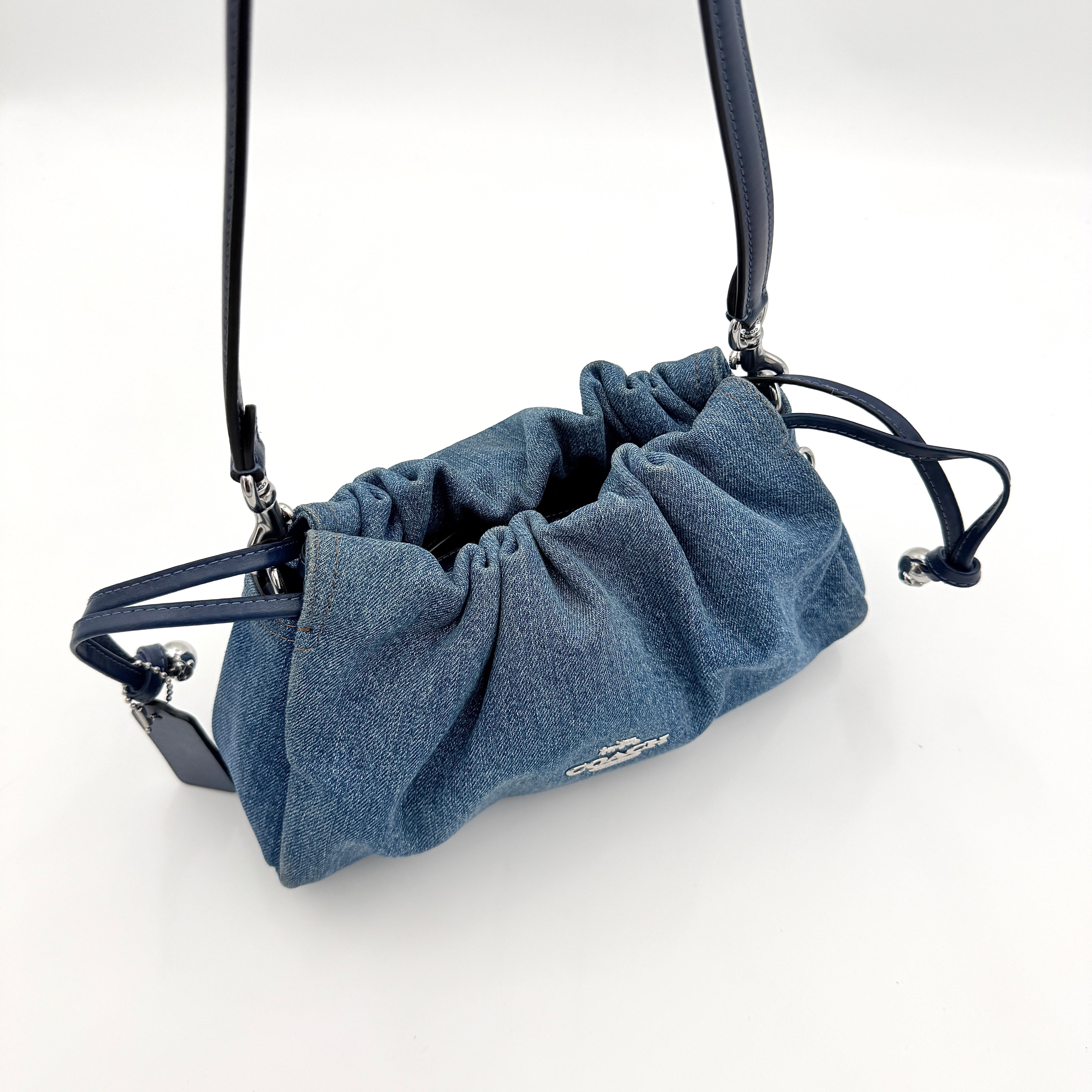 Coach Faye Shoulder Bag in blue denim with navy leather strap and detachable crossbody, styled simply against a white background.