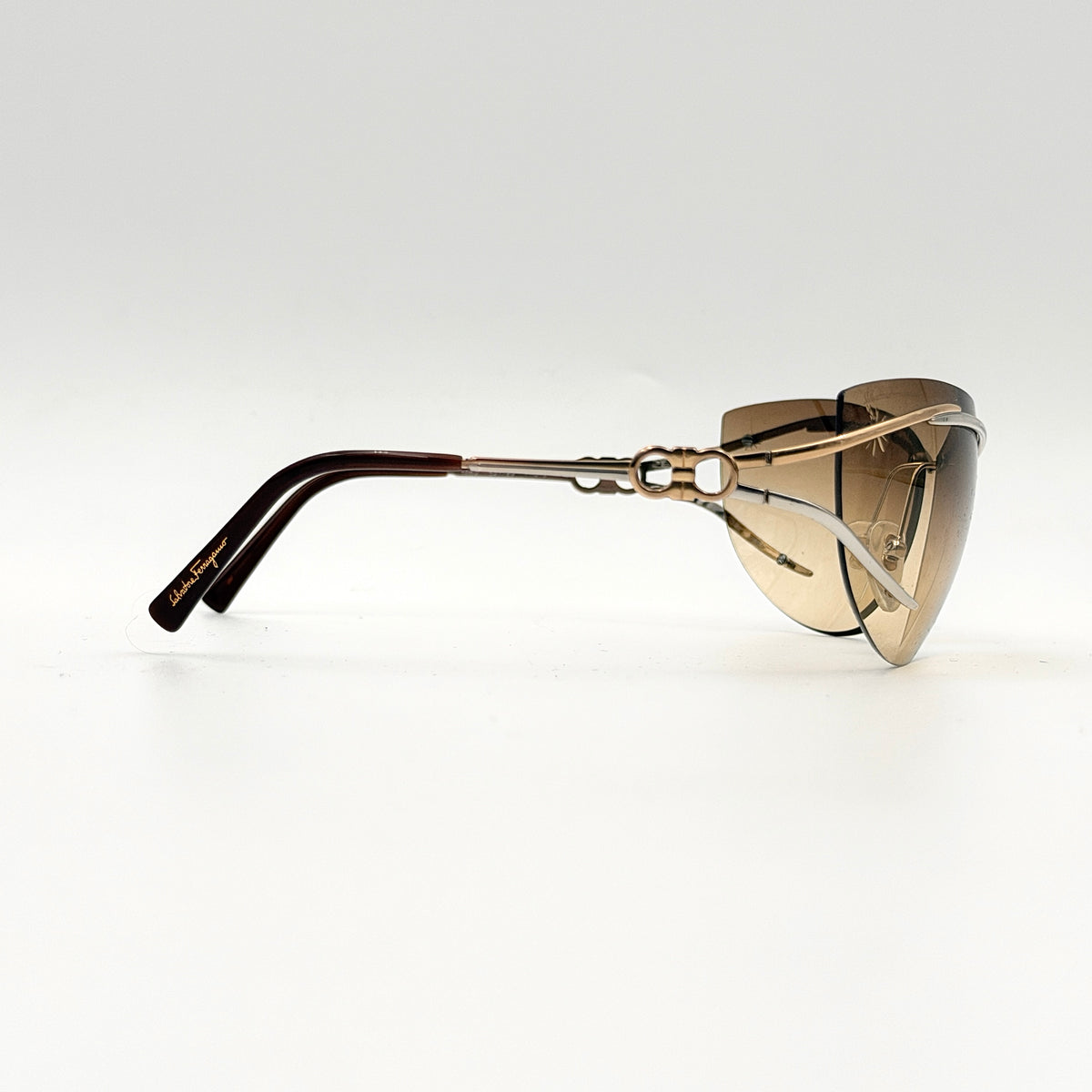 Salvatore Ferragamo rimless sunglasses with gradient brown lenses and sculptural Gancini metal arms on a white background.