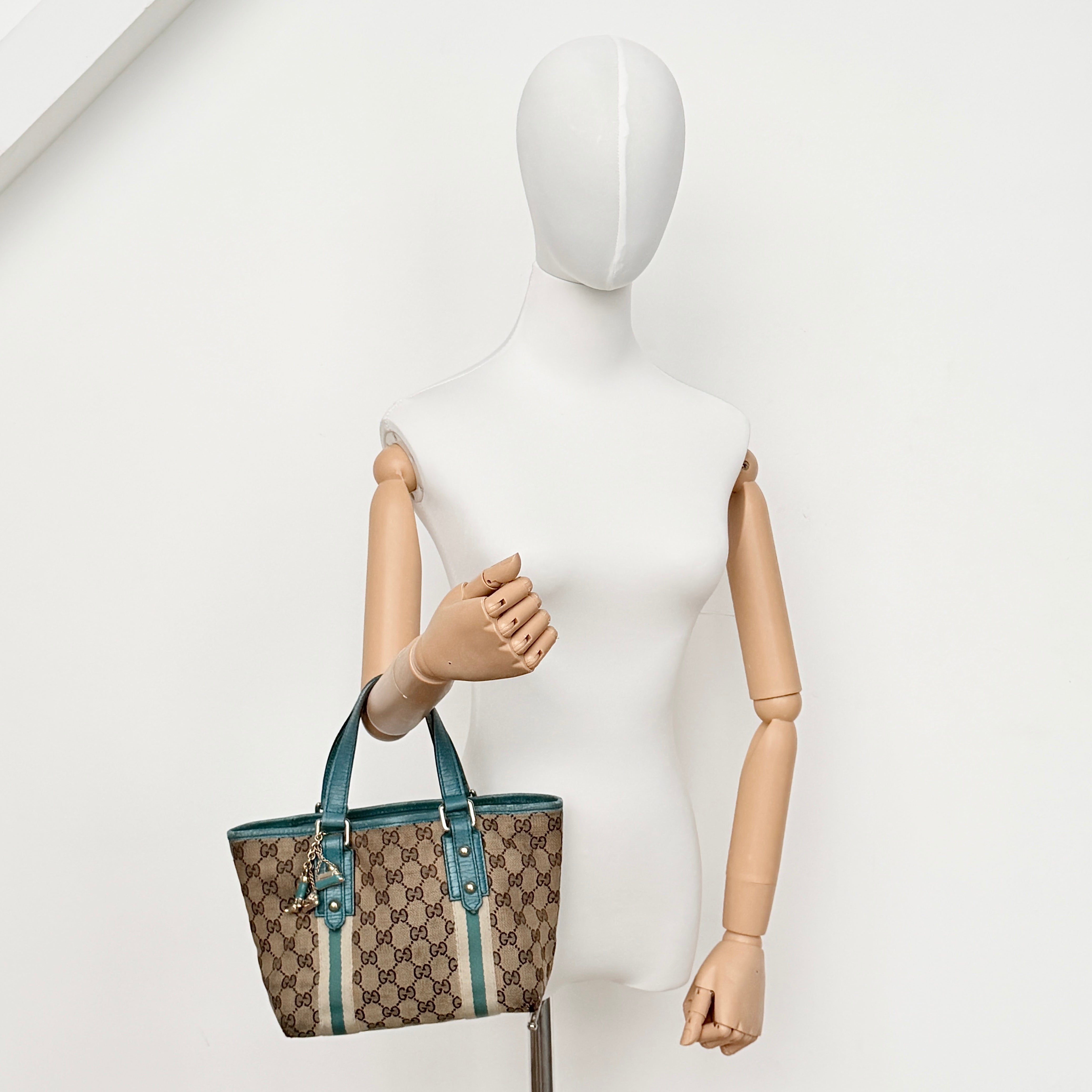 Gucci GG Monogram Jolicoeur Mini Shoulder Bag in beige canvas with teal blue leather trim and gold hardware, shown with a playful charm.