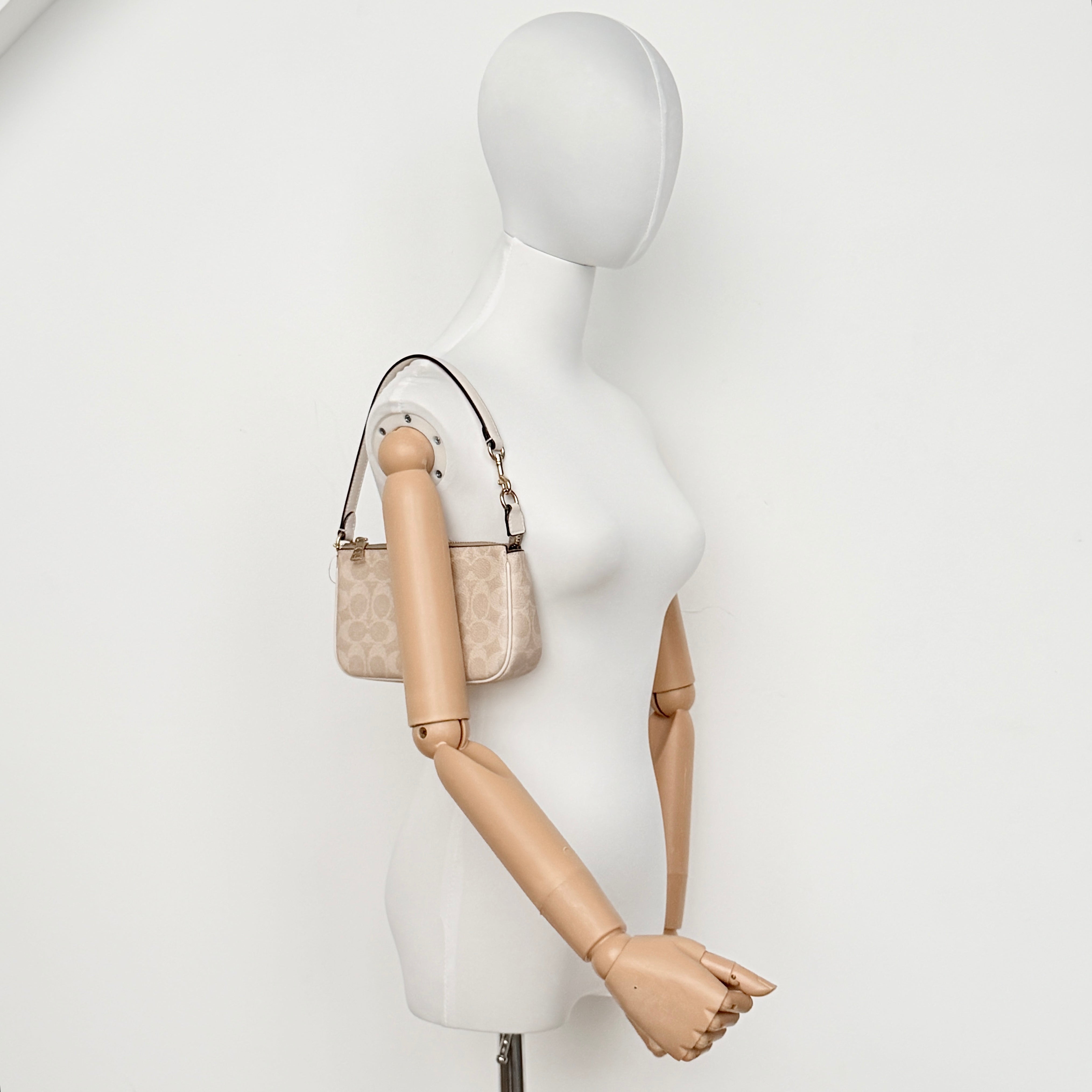 Coach Signature Nolita 19 Shoulder Bag in beige and white canvas with gold-tone hardware and detachable strap, photographed against a plain backdrop.