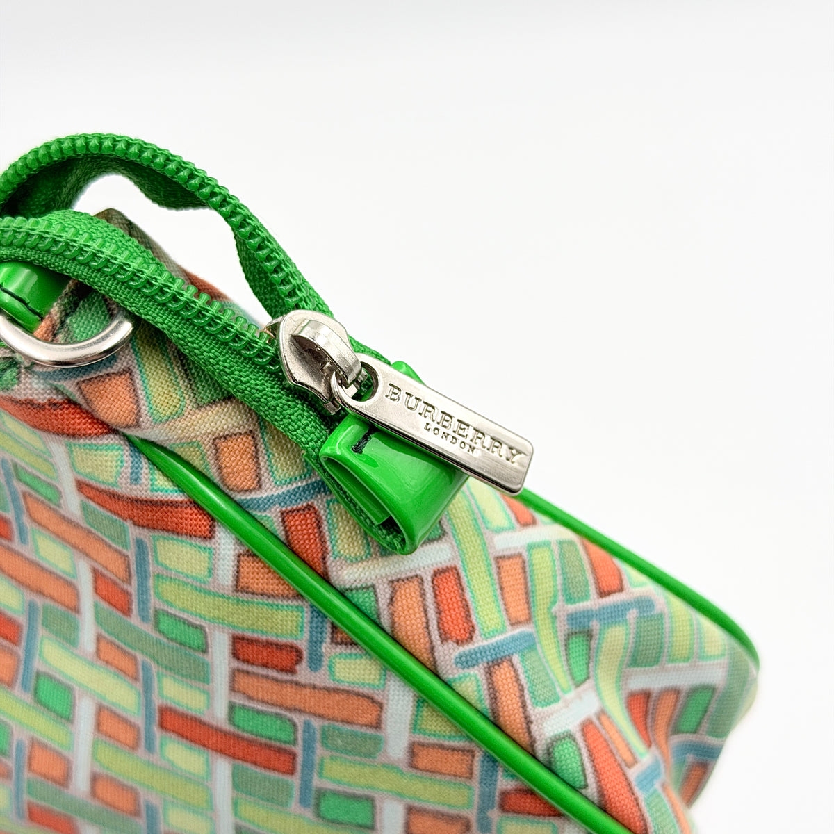 Burberry Blue Label geometric pouch in multicolor canvas with green trim and zip closure, photographed against a clean white background.