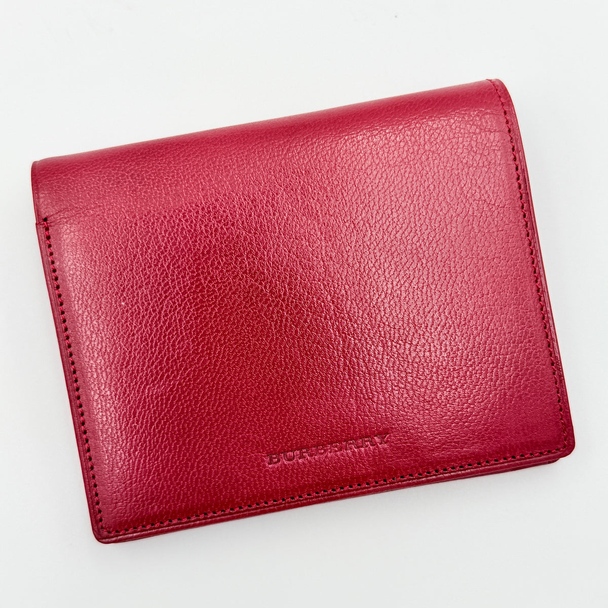Burberry Nova Check bifold wallet in grained red leather with signature tartan interior, shown closed against a white background