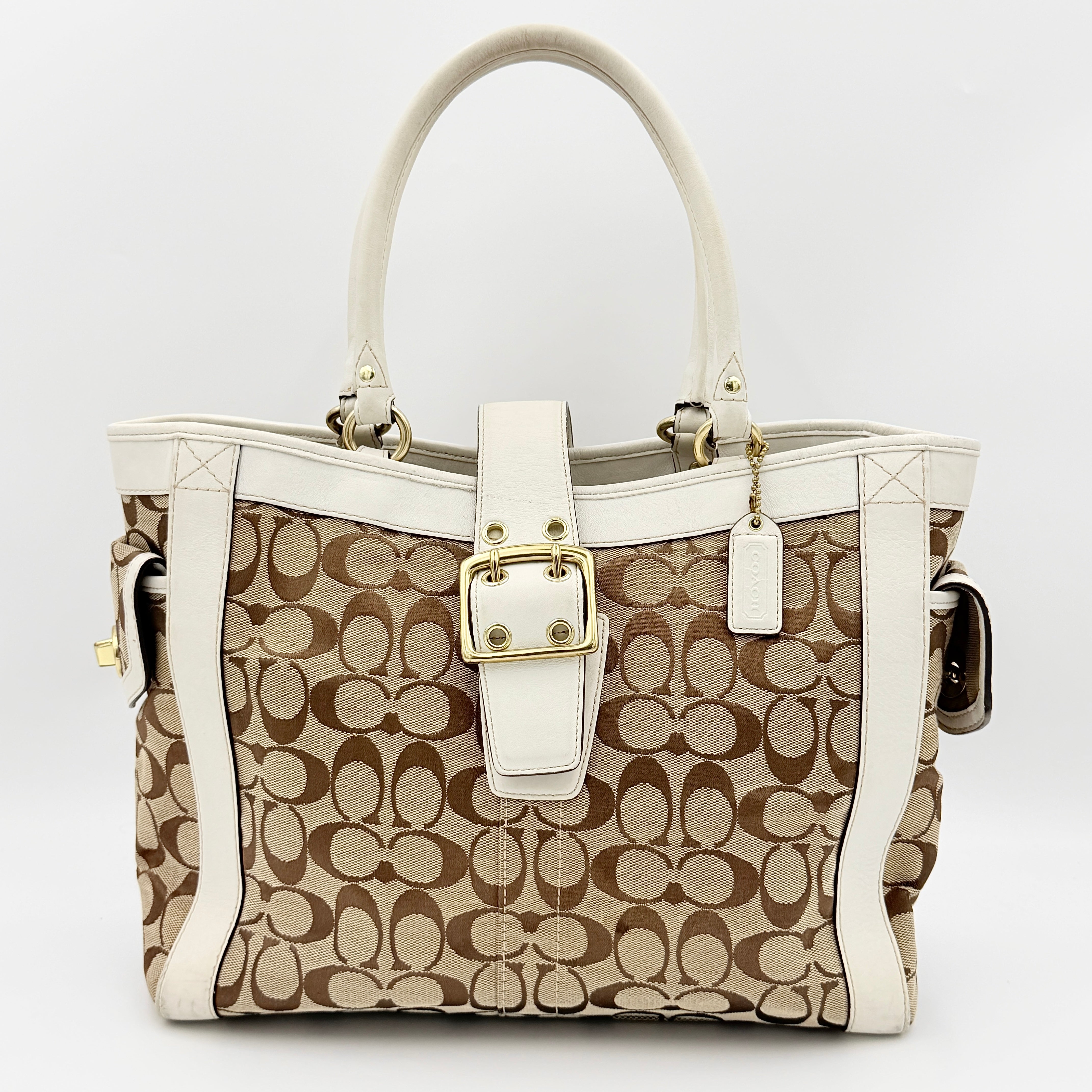 Coach Signature Soho Buckle Tote in beige canvas with white leather trim and gold-tone hardware, displayed against a clean background.