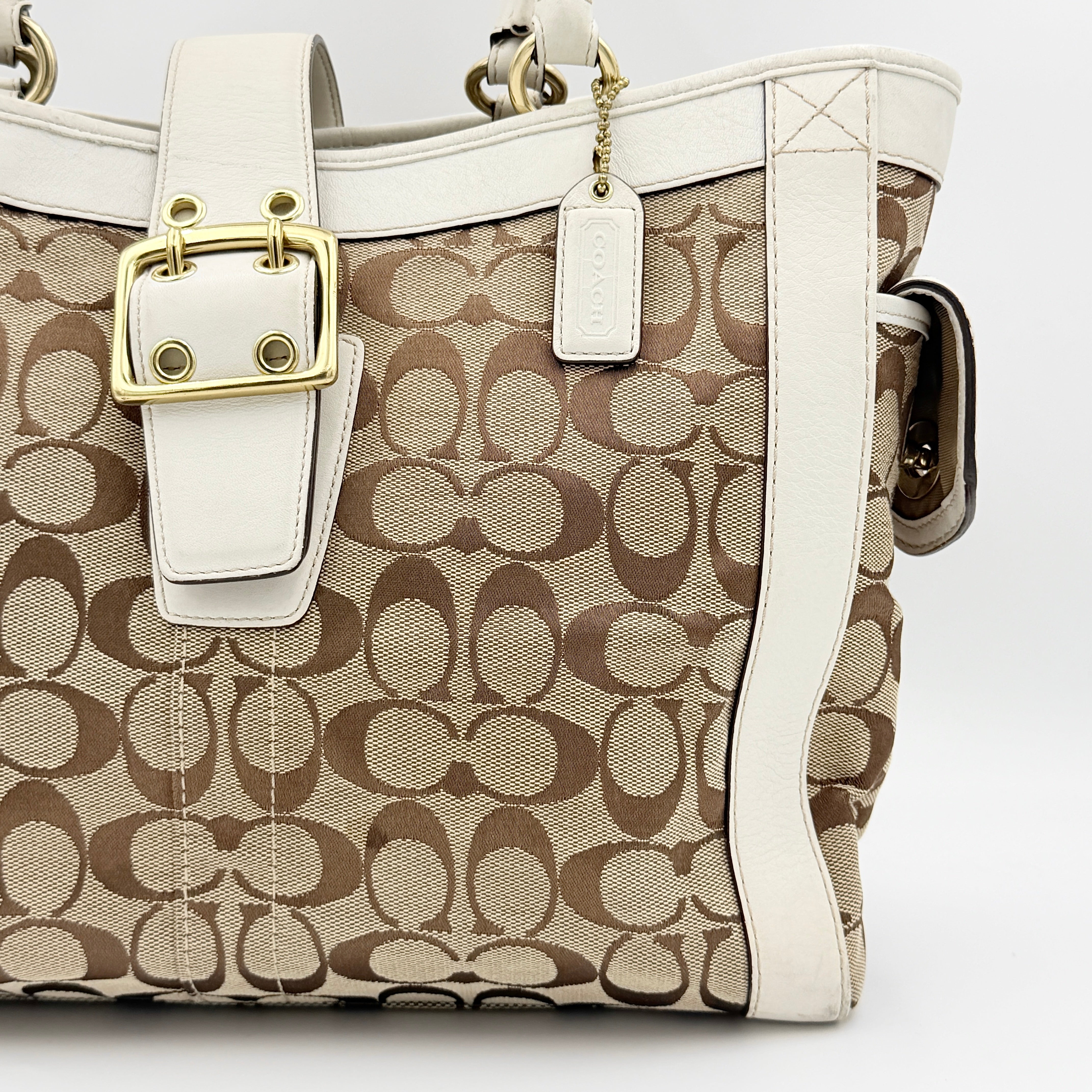 Coach Signature Soho Buckle Tote in beige canvas with white leather trim and gold-tone hardware, displayed against a clean background.
