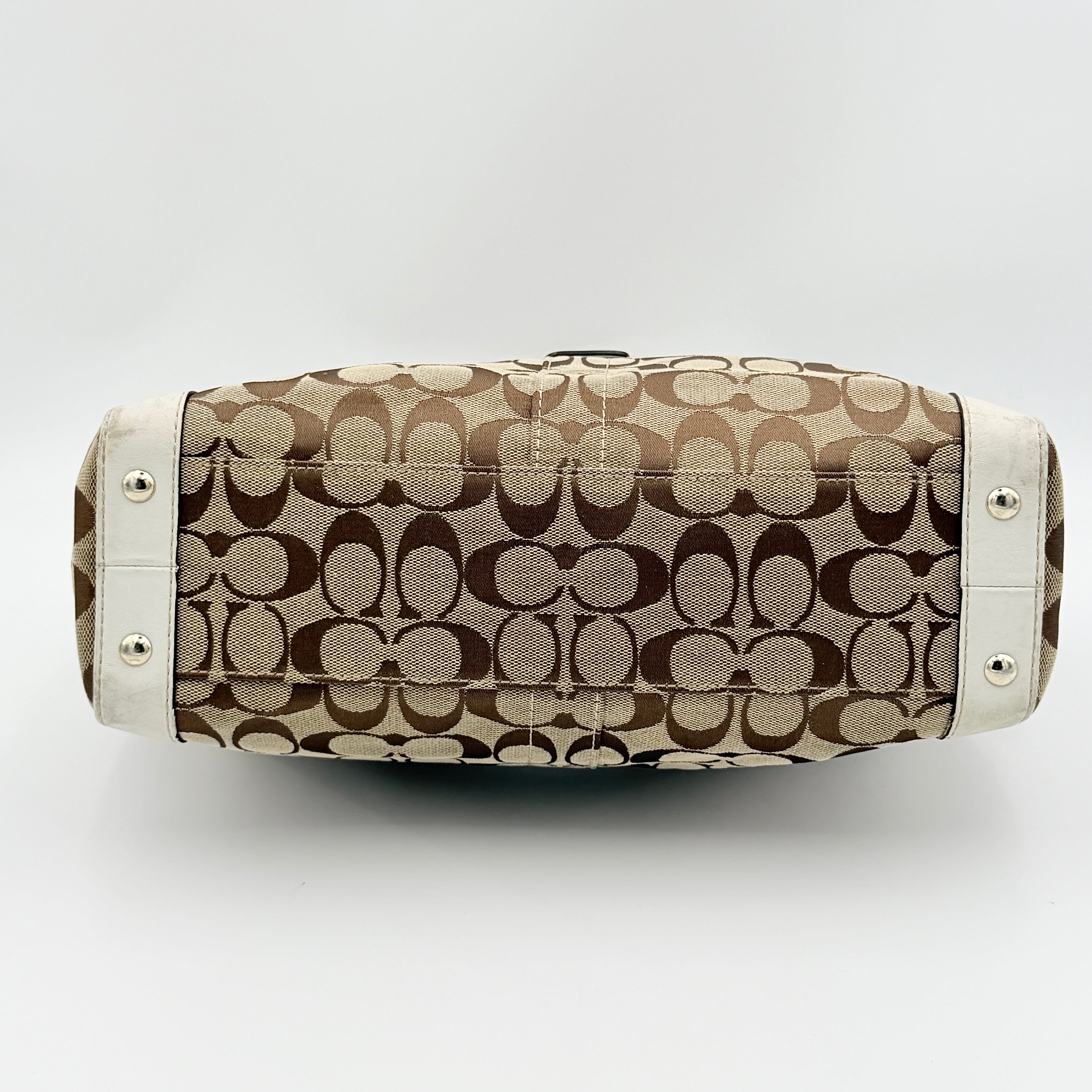Coach Signature Soho Buckle Tote in beige canvas with white leather trim and gold-tone hardware, displayed against a clean background.