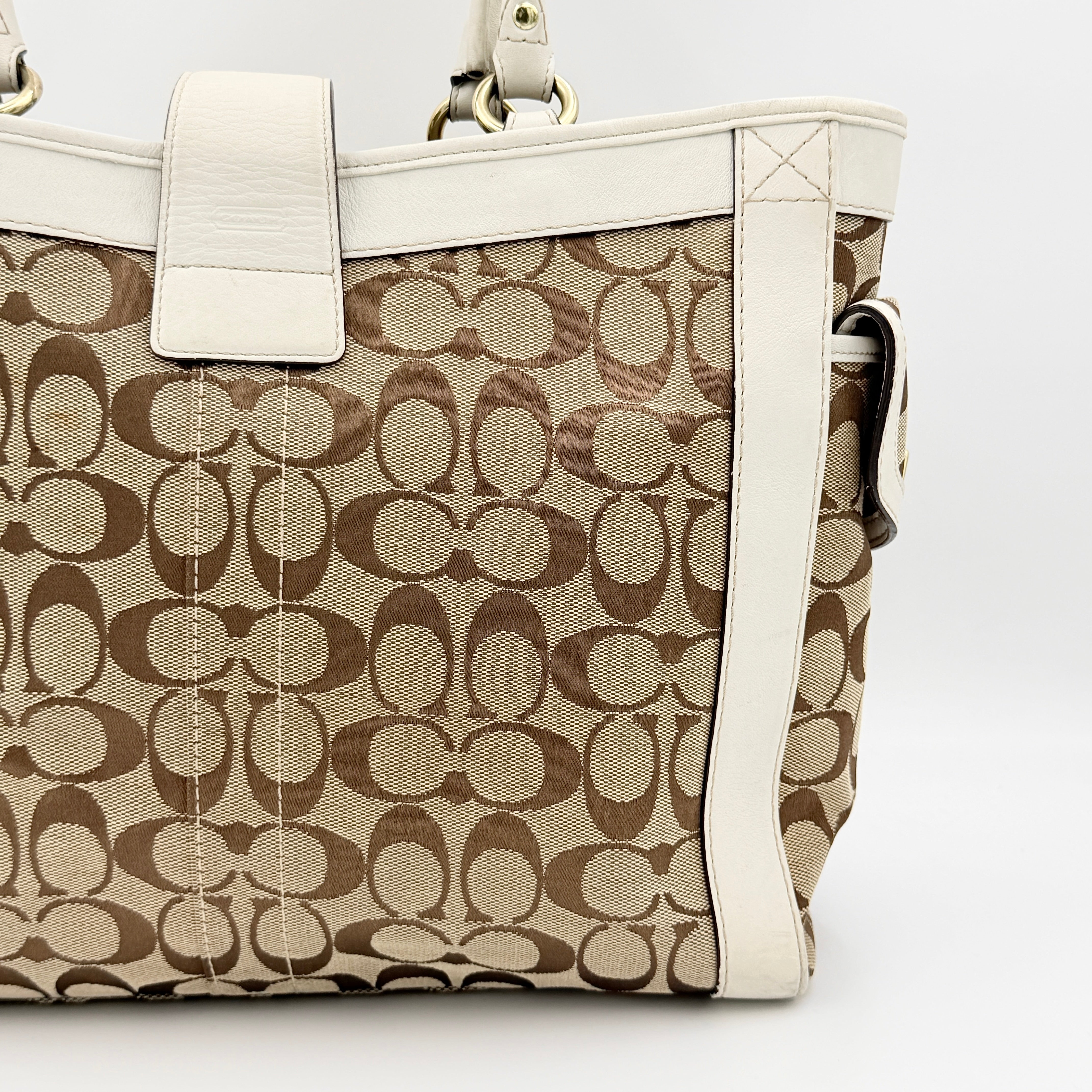 Coach Signature Soho Buckle Tote in beige canvas with white leather trim and gold-tone hardware, displayed against a clean background.