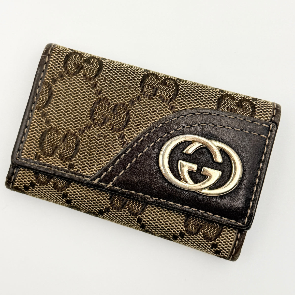 Gucci GG monogram canvas key case in brown with leather trim and a silver GG emblem on the front.