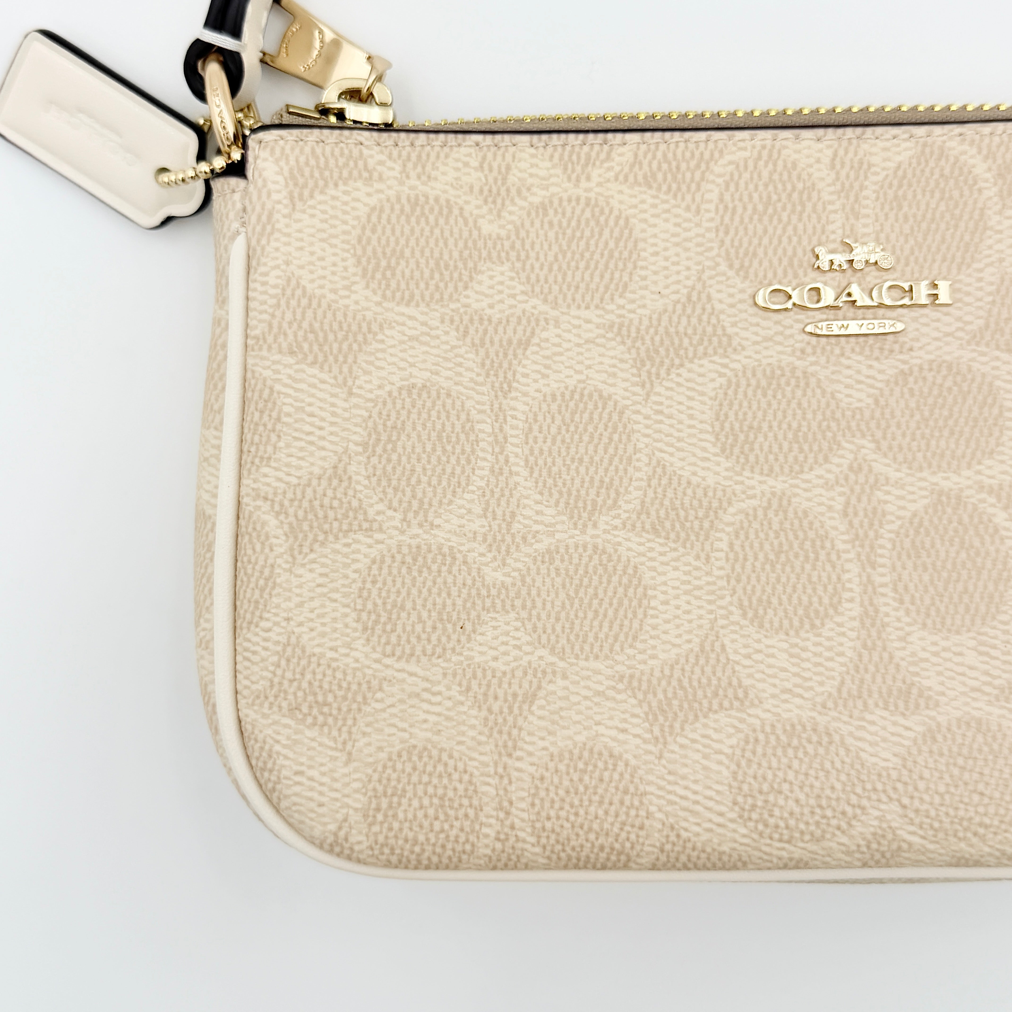Coach Signature Nolita 19 Shoulder Bag in beige and white canvas with gold-tone hardware and detachable strap, photographed against a plain backdrop.