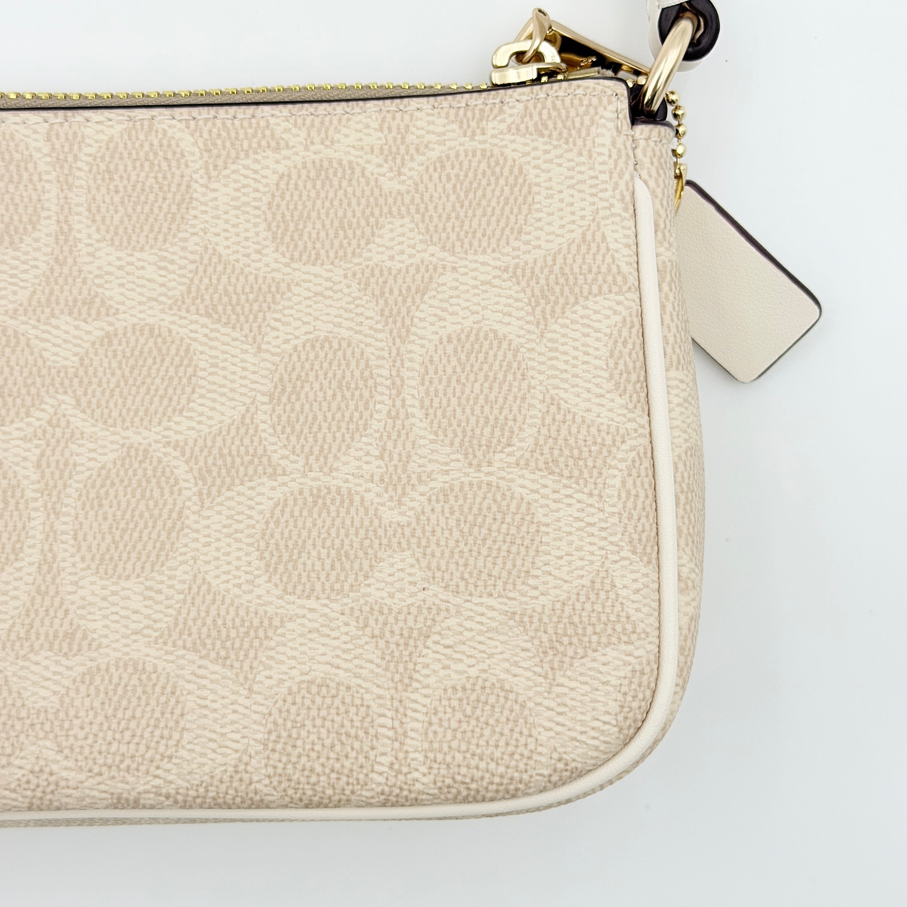 Coach Signature Nolita 19 Shoulder Bag in beige and white canvas with gold-tone hardware and detachable strap, photographed against a plain backdrop.