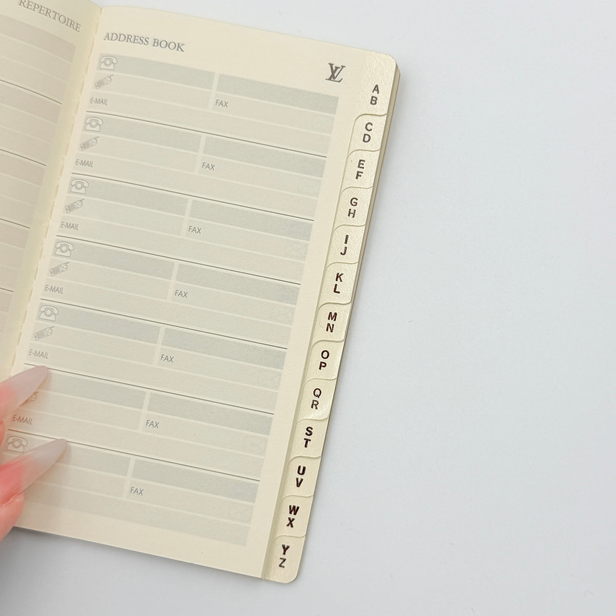 Louis Vuitton Répertoire Address Book in cream with black logo, displayed on a clean white background.