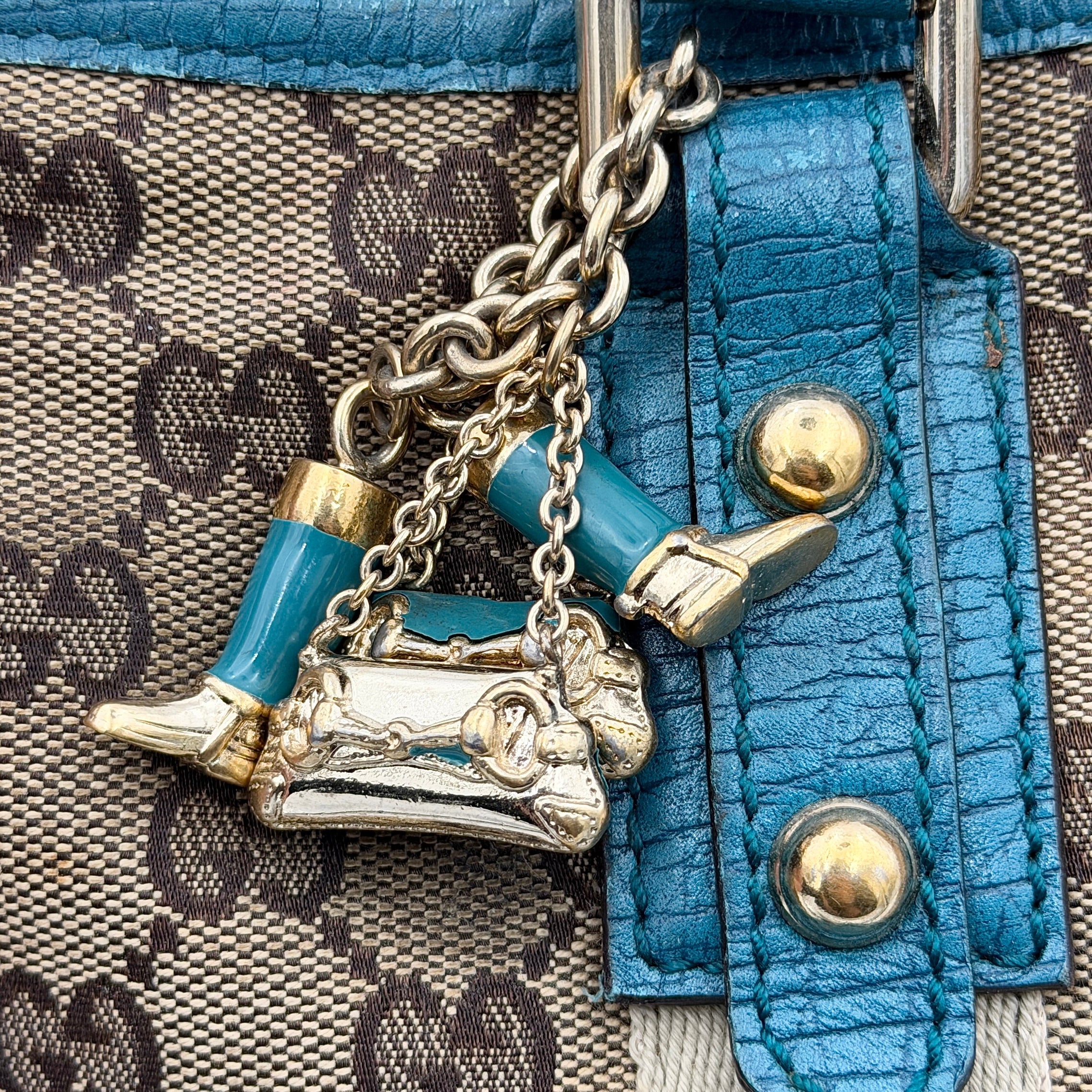 Gucci GG Monogram Jolicoeur Mini Shoulder Bag in beige canvas with teal blue leather trim and gold hardware, shown with a playful charm.