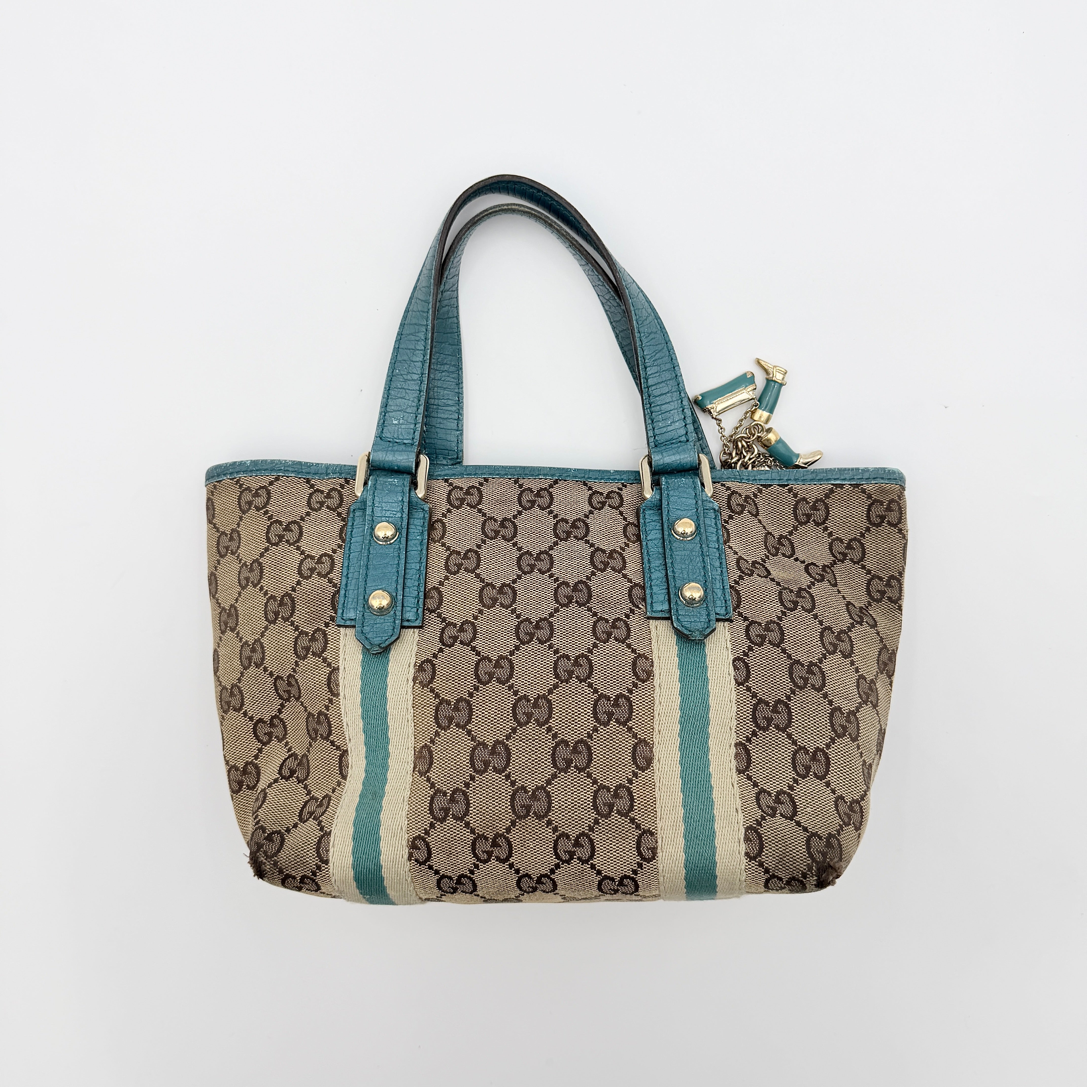 Gucci GG Monogram Jolicoeur Mini Shoulder Bag in beige canvas with teal blue leather trim and gold hardware, shown with a playful charm.