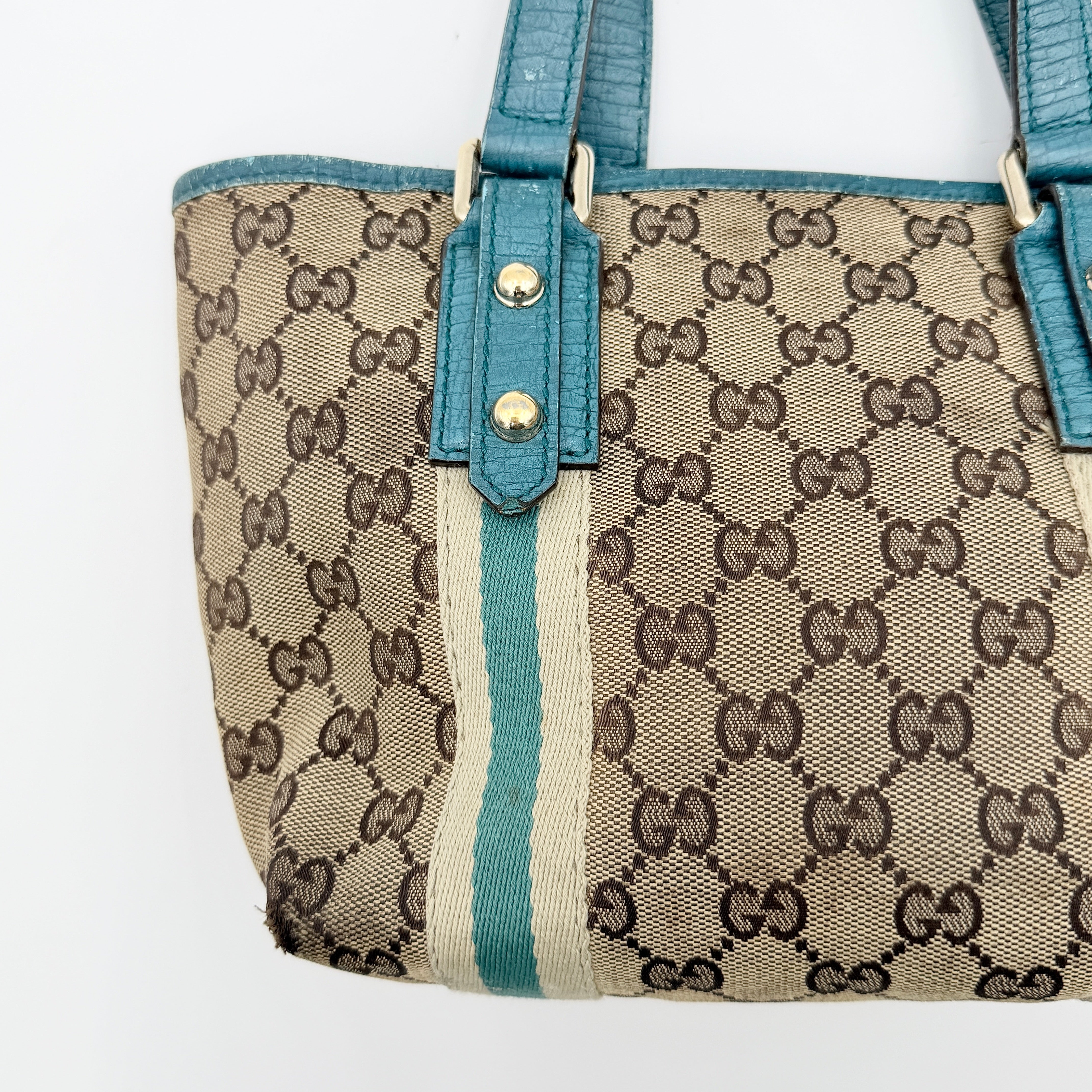 Gucci GG Monogram Jolicoeur Mini Shoulder Bag in beige canvas with teal blue leather trim and gold hardware, shown with a playful charm.