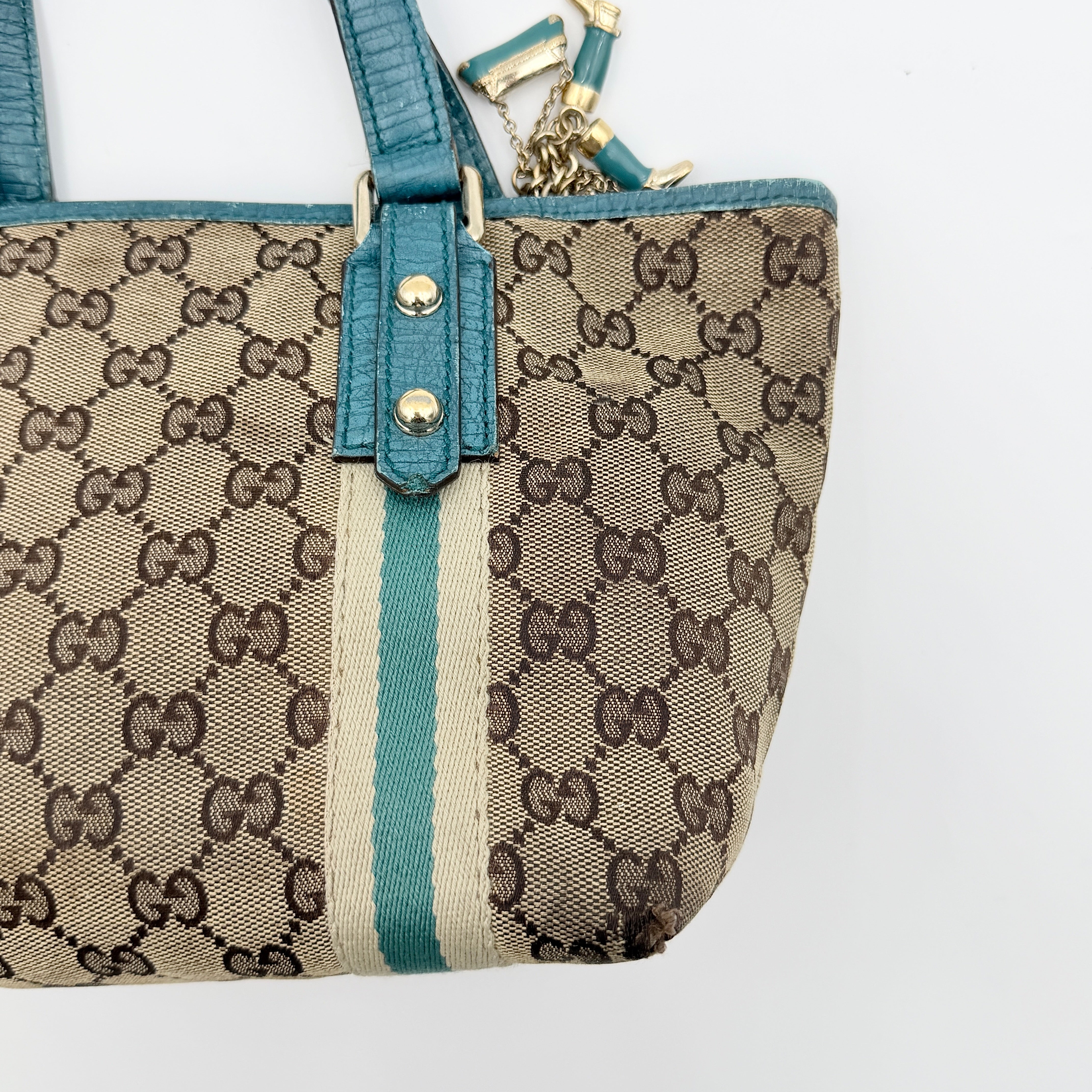 Gucci GG Monogram Jolicoeur Mini Shoulder Bag in beige canvas with teal blue leather trim and gold hardware, shown with a playful charm.