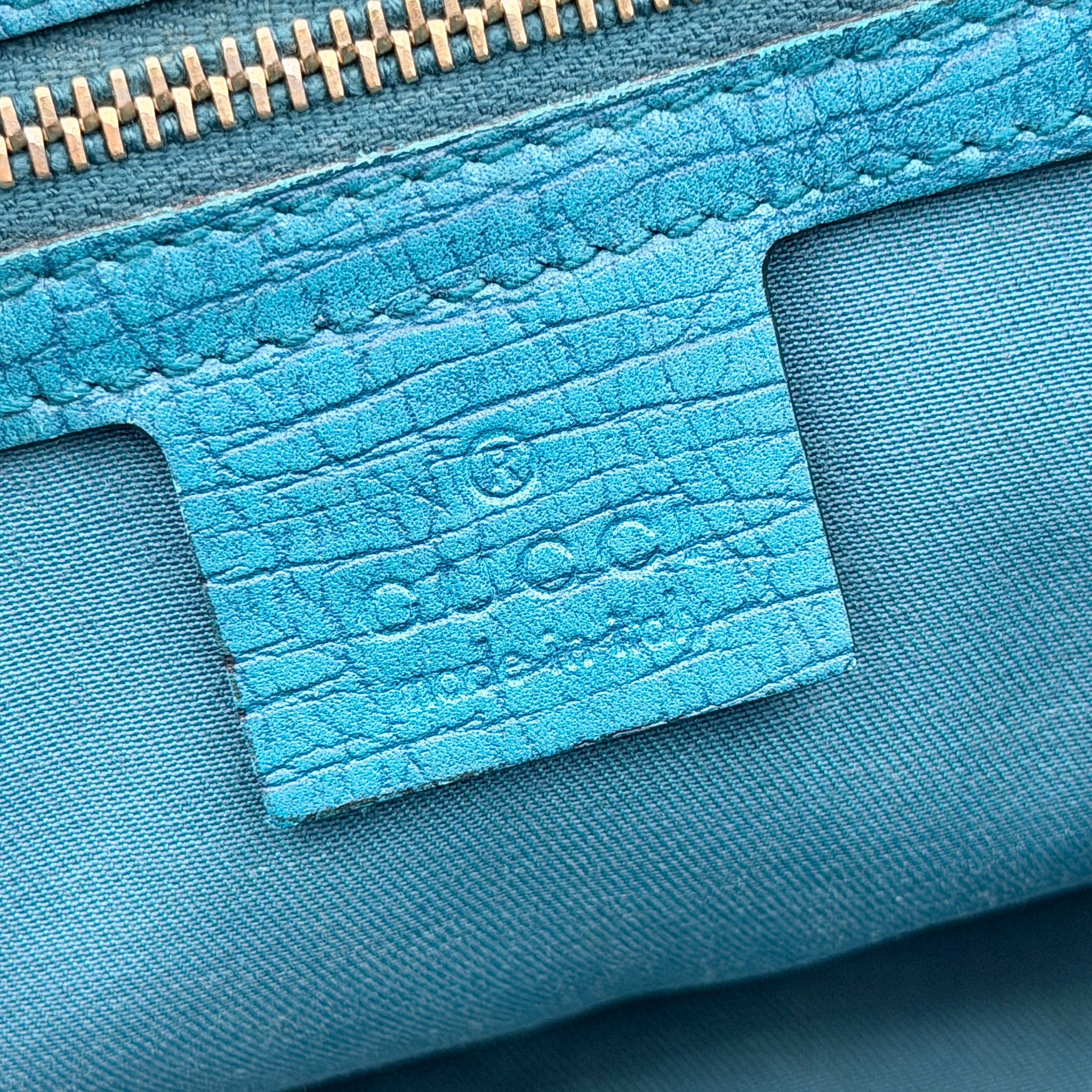 Gucci GG Monogram Jolicoeur Mini Shoulder Bag in beige canvas with teal blue leather trim and gold hardware, shown with a playful charm.