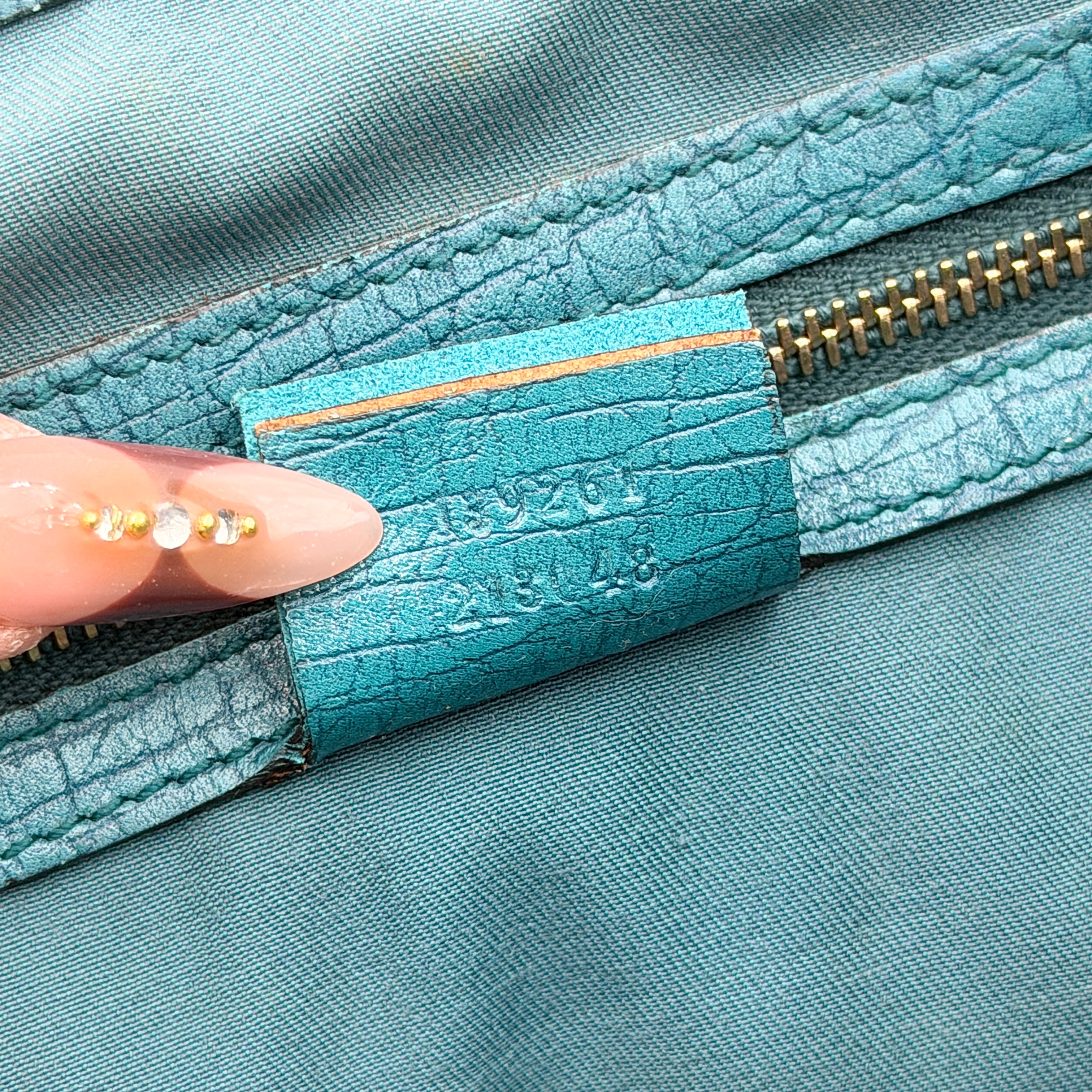 Gucci GG Monogram Jolicoeur Mini Shoulder Bag in beige canvas with teal blue leather trim and gold hardware, shown with a playful charm.