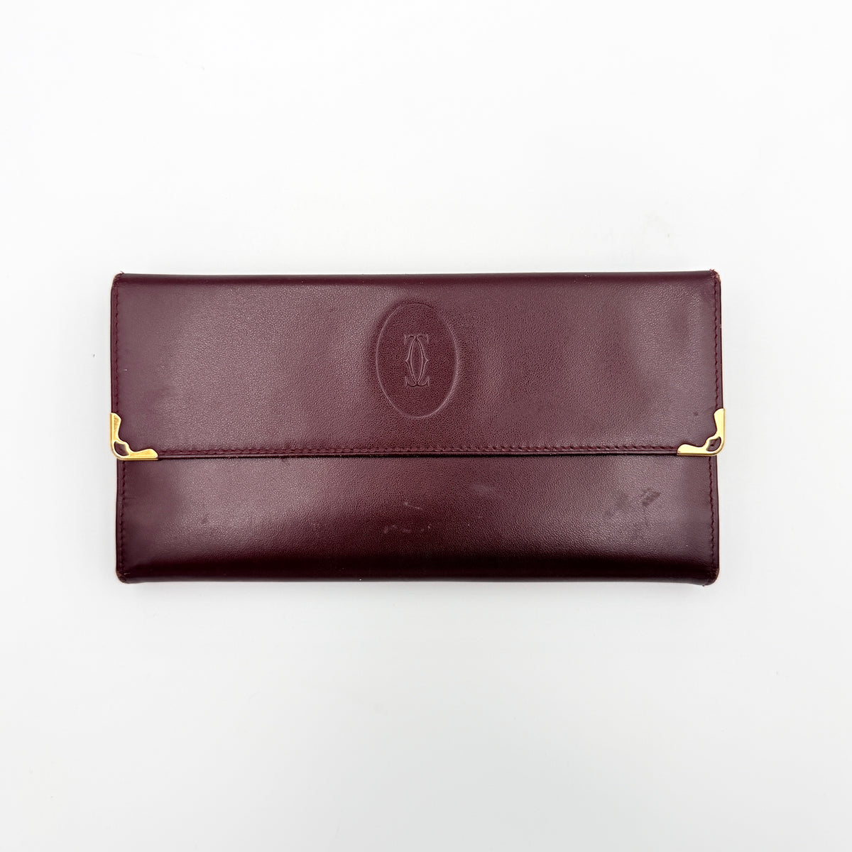 Cartier Must de Cartier trifold wallet in burgundy leather with gold-tone corners, showing the embossed double C logo on the front flap.