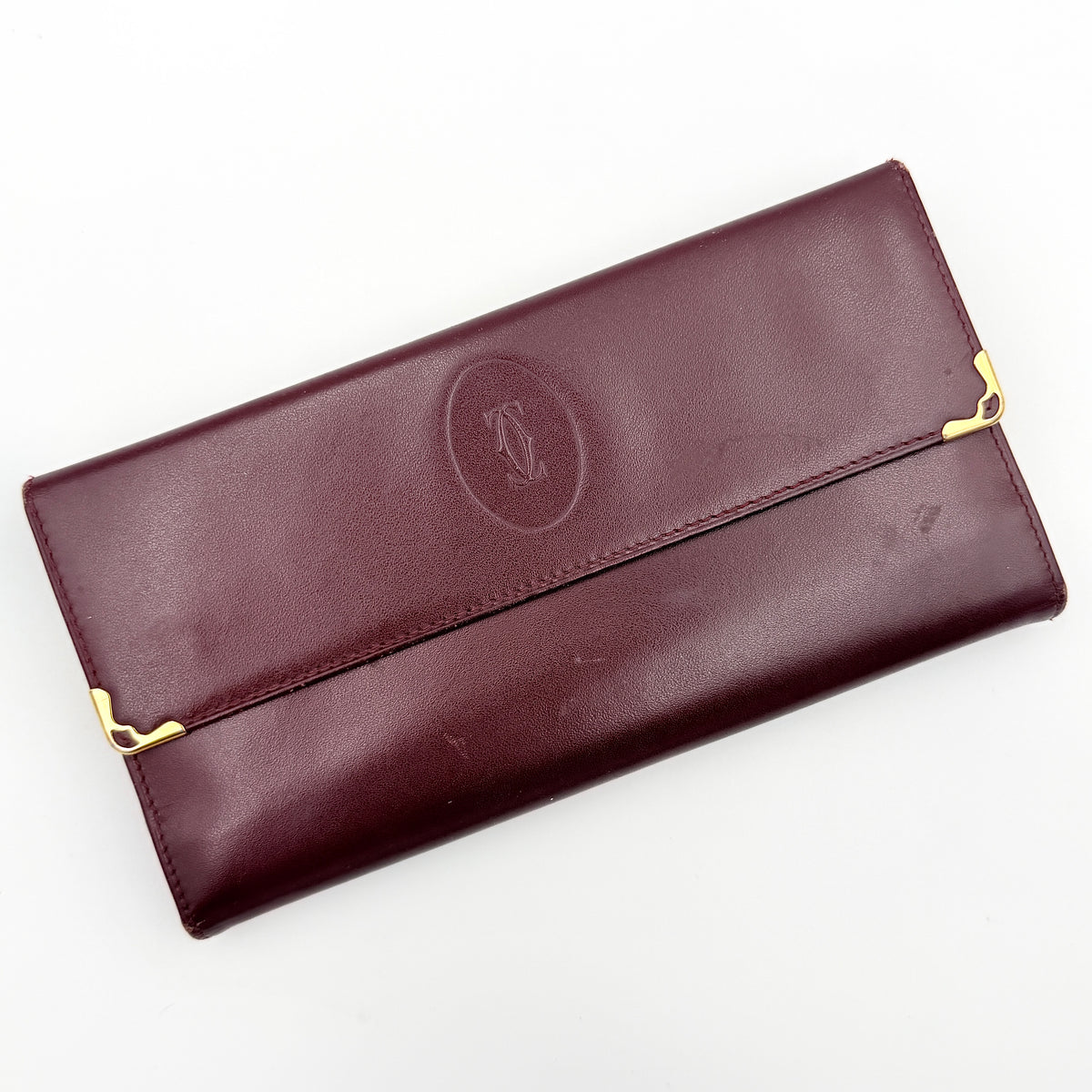 Cartier Must de Cartier trifold wallet in burgundy leather with gold-tone corners, showing the embossed double C logo on the front flap.