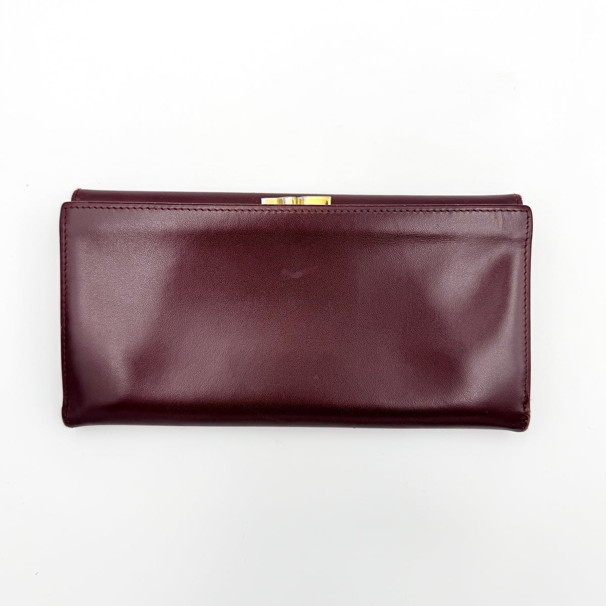 Cartier Must de Cartier trifold wallet in burgundy leather with gold-tone corners, showing the embossed double C logo on the front flap.