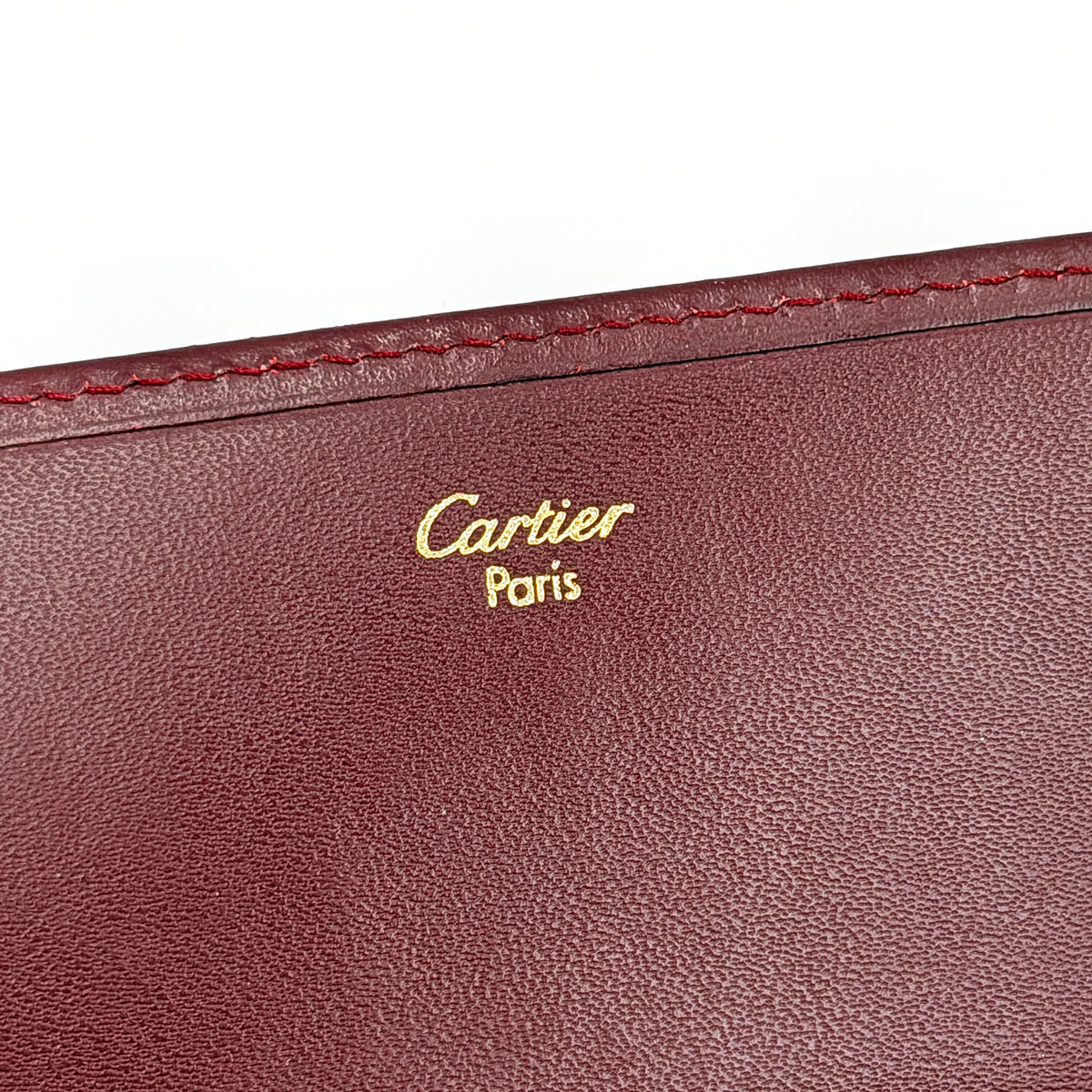 Cartier Must de Cartier trifold wallet in burgundy leather with gold-tone corners, showing the embossed double C logo on the front flap.