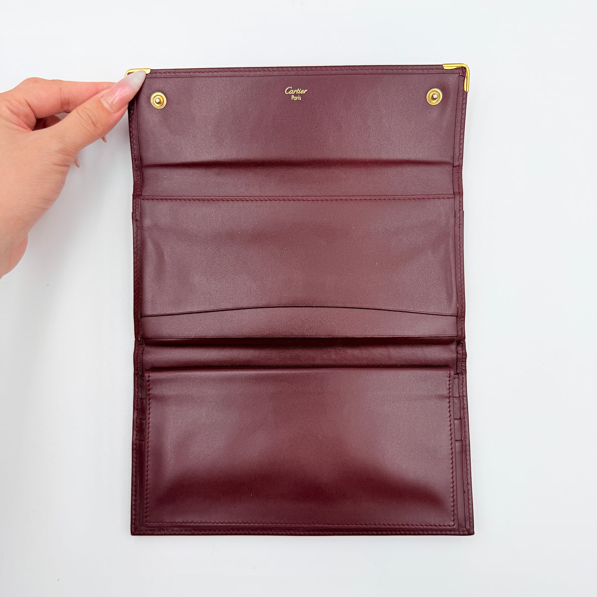 Cartier Must de Cartier trifold wallet in burgundy leather with gold-tone corners, showing the embossed double C logo on the front flap.