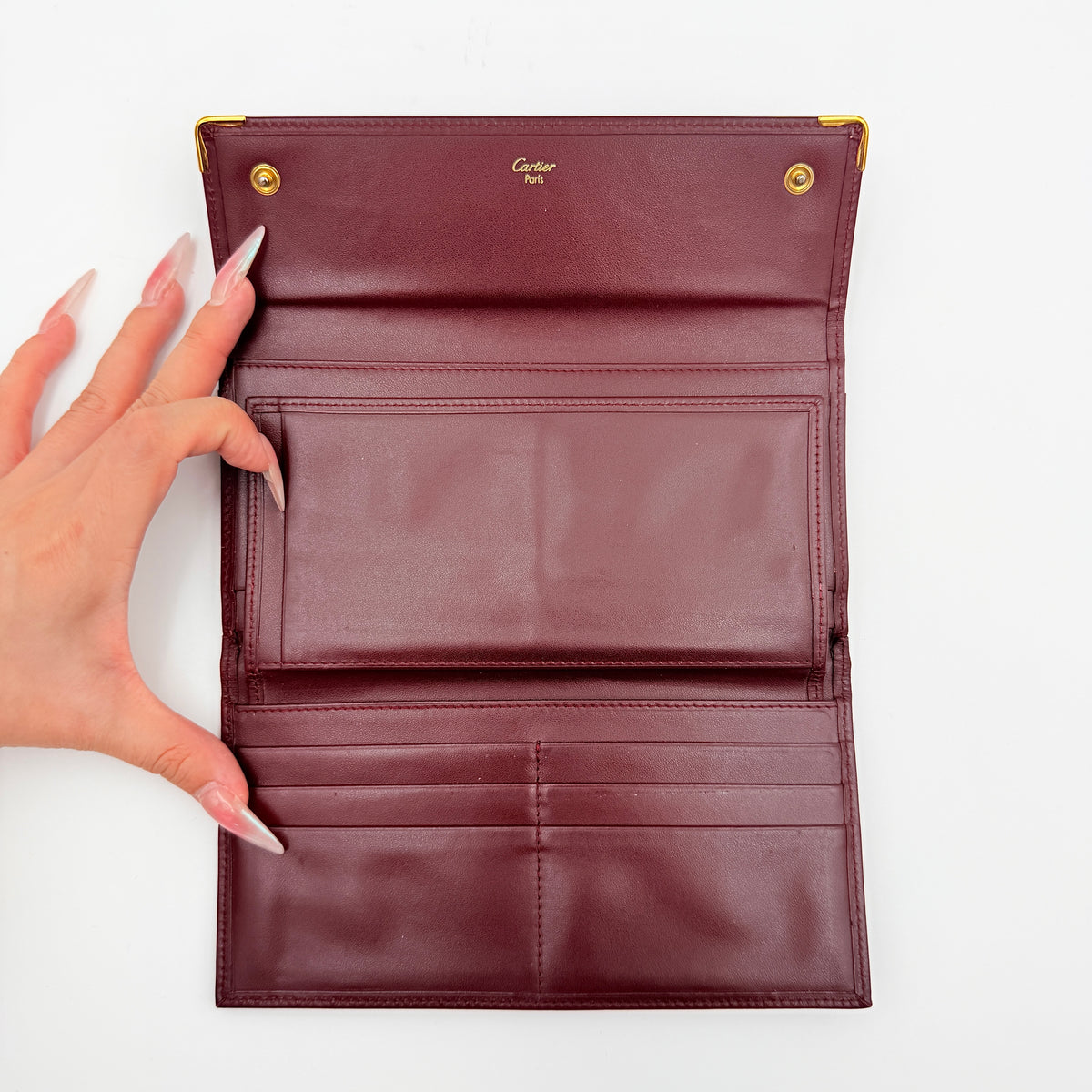 Cartier Must de Cartier trifold wallet in burgundy leather with gold-tone corners, showing the embossed double C logo on the front flap.