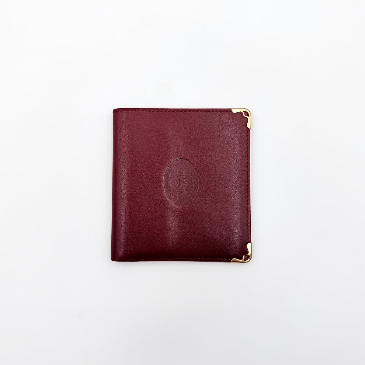 Cartier Must de Cartier bifold wallet in burgundy leather with gold-tone corner hardware and embossed logo, shown with authenticity card.