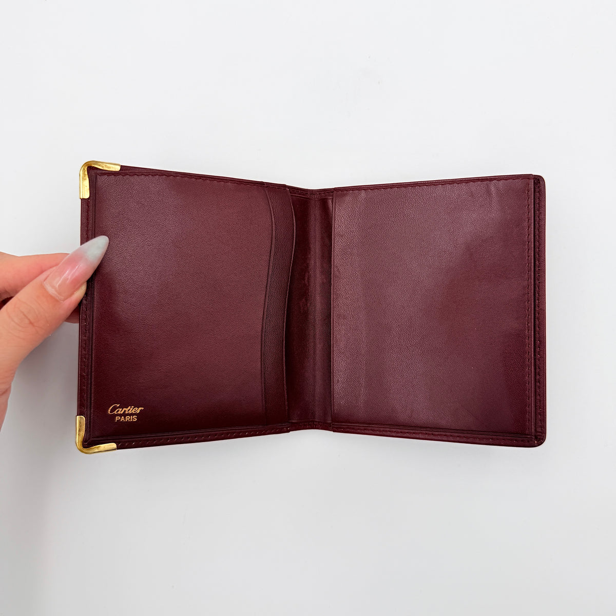 Cartier Must de Cartier bifold wallet in burgundy leather with gold-tone corner hardware and embossed logo, shown with authenticity card.