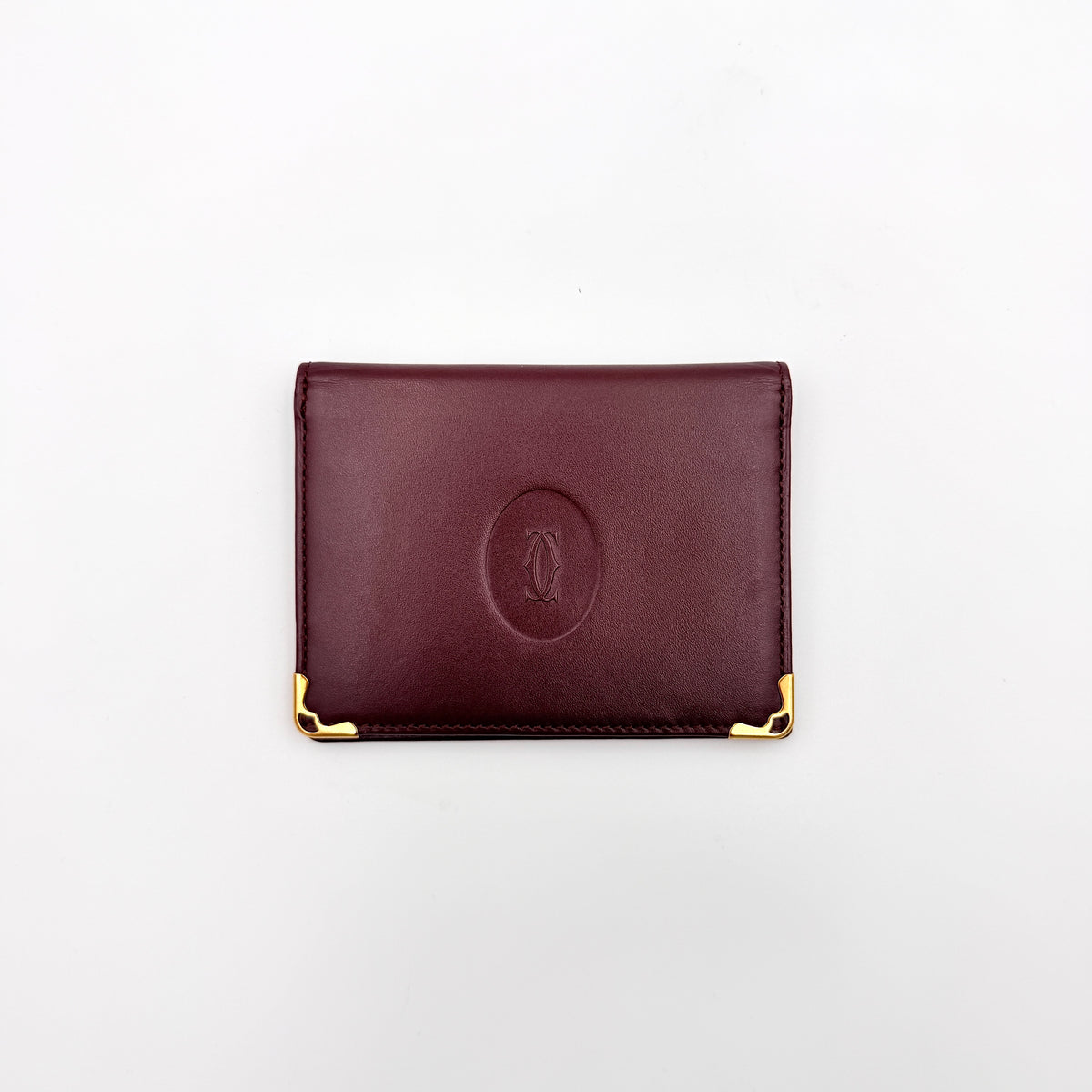 Cartier Must de Cartier card case in rich burgundy leather with gold-tone corner details and an embossed logo.