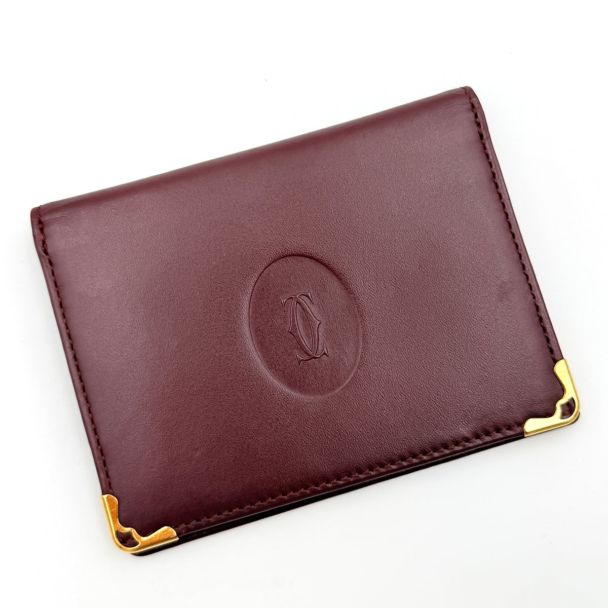 Cartier Must de Cartier card case in rich burgundy leather with gold-tone corner details and an embossed logo.