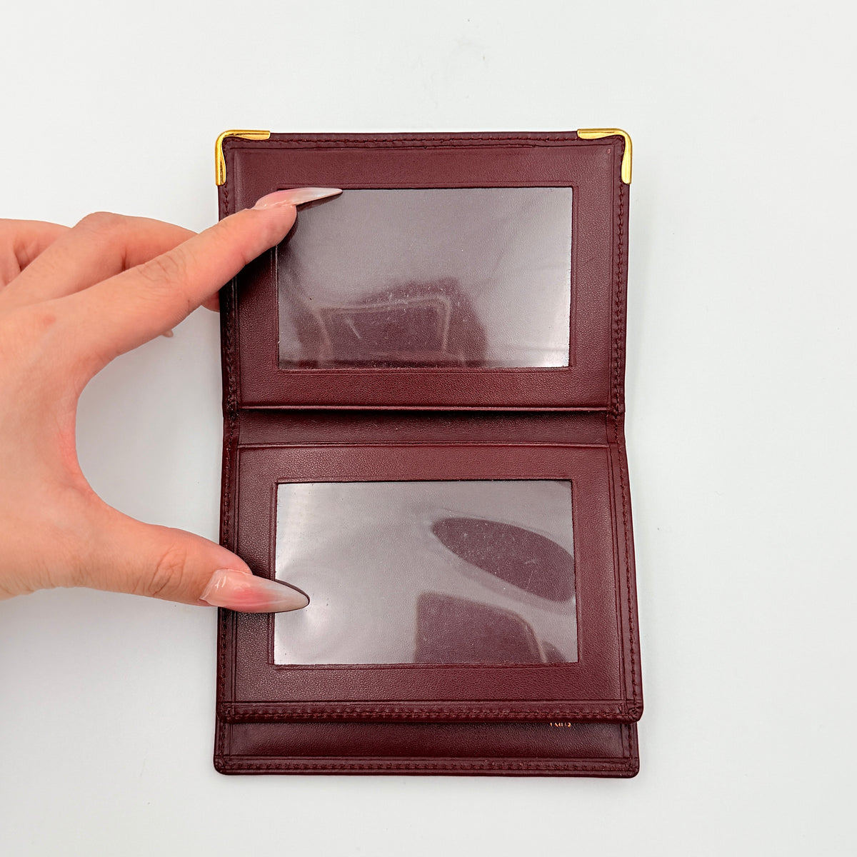 Cartier Must de Cartier card case in rich burgundy leather with gold-tone corner details and an embossed logo.