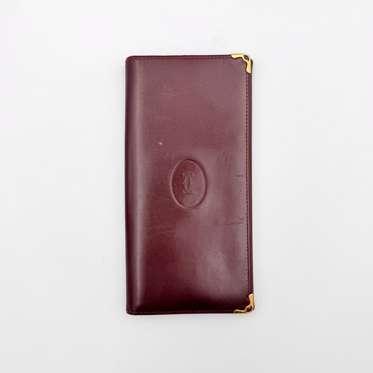 Cartier Must de Cartier bifold long wallet in burgundy leather with gold-tone corners.