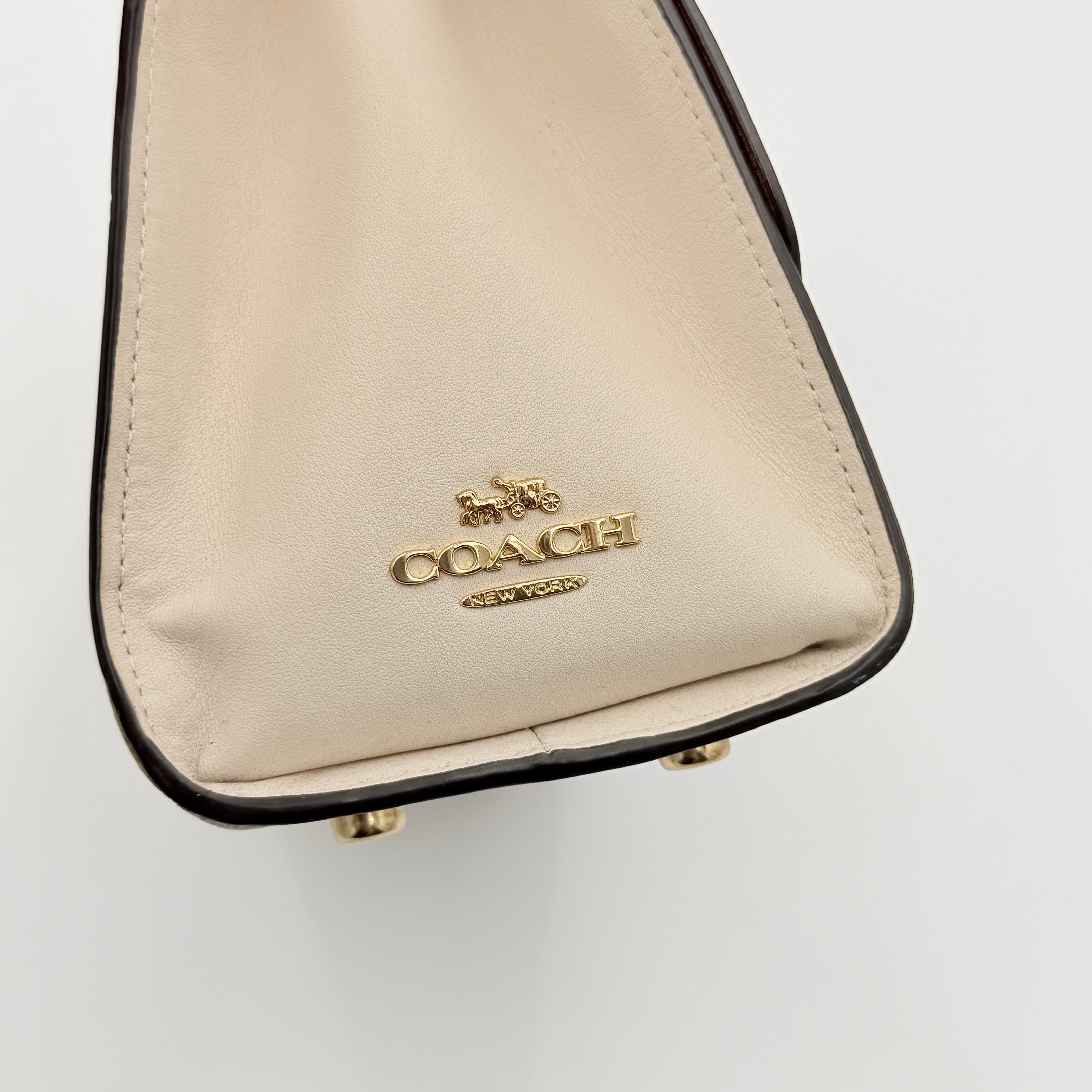 Coach Signature Tilly Top Handle Bag in beige and white with gold-tone hardware and detachable strap, displayed against a clean background.