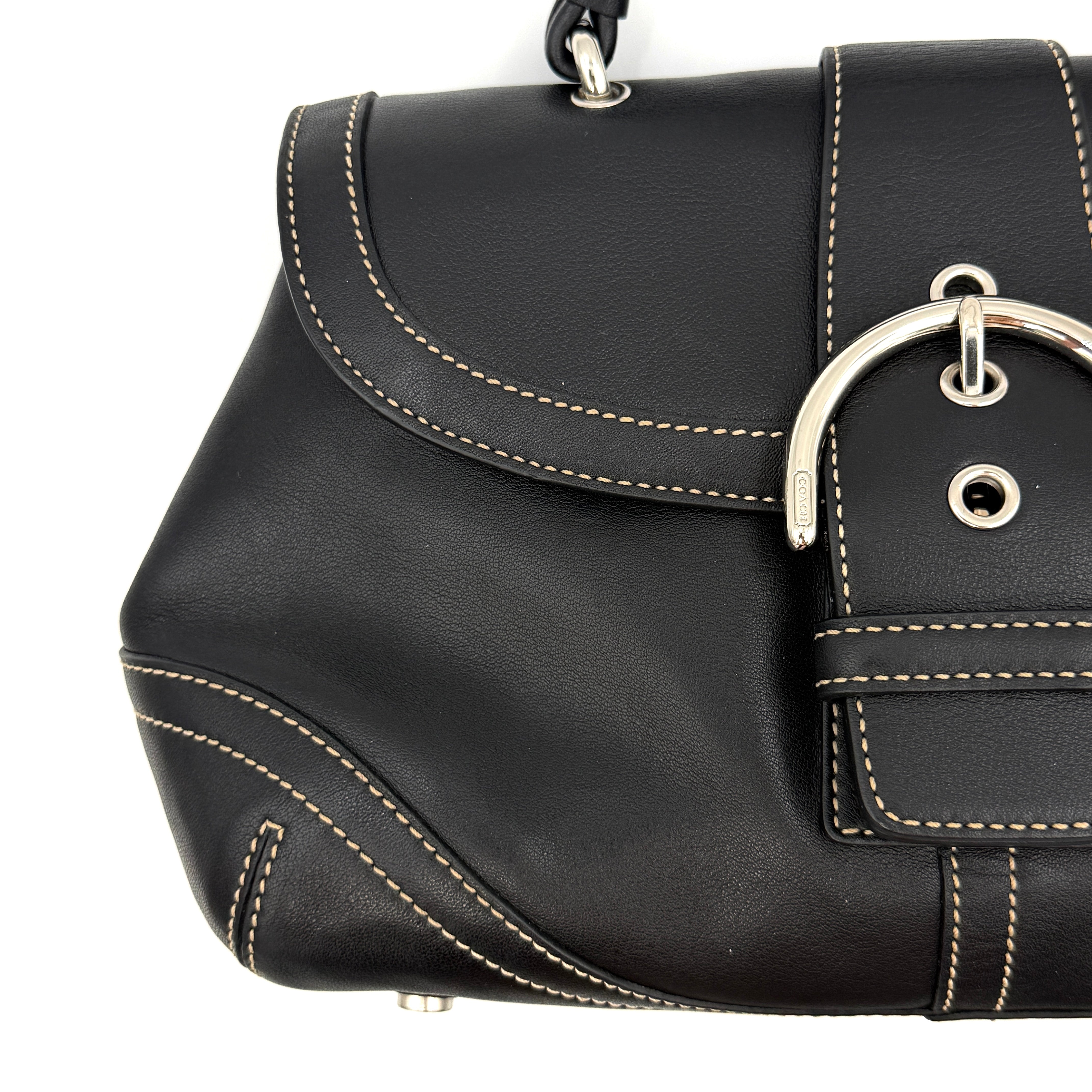 Coach Soho Buckle Top Handle Bag in black leather with contrast stitching and silver buckle, presented against a white background.