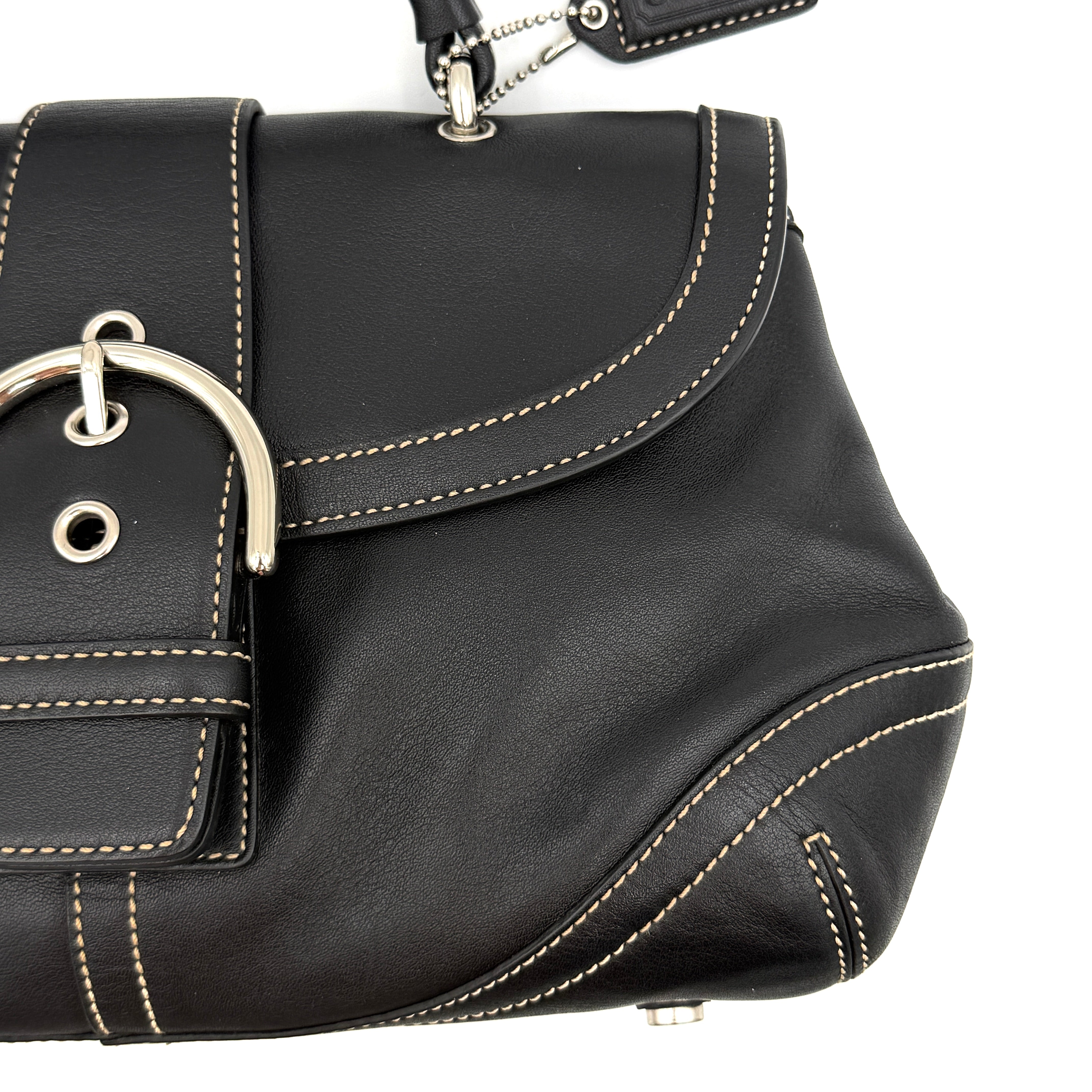 Coach Soho Buckle Top Handle Bag in black leather with contrast stitching and silver buckle, presented against a white background.