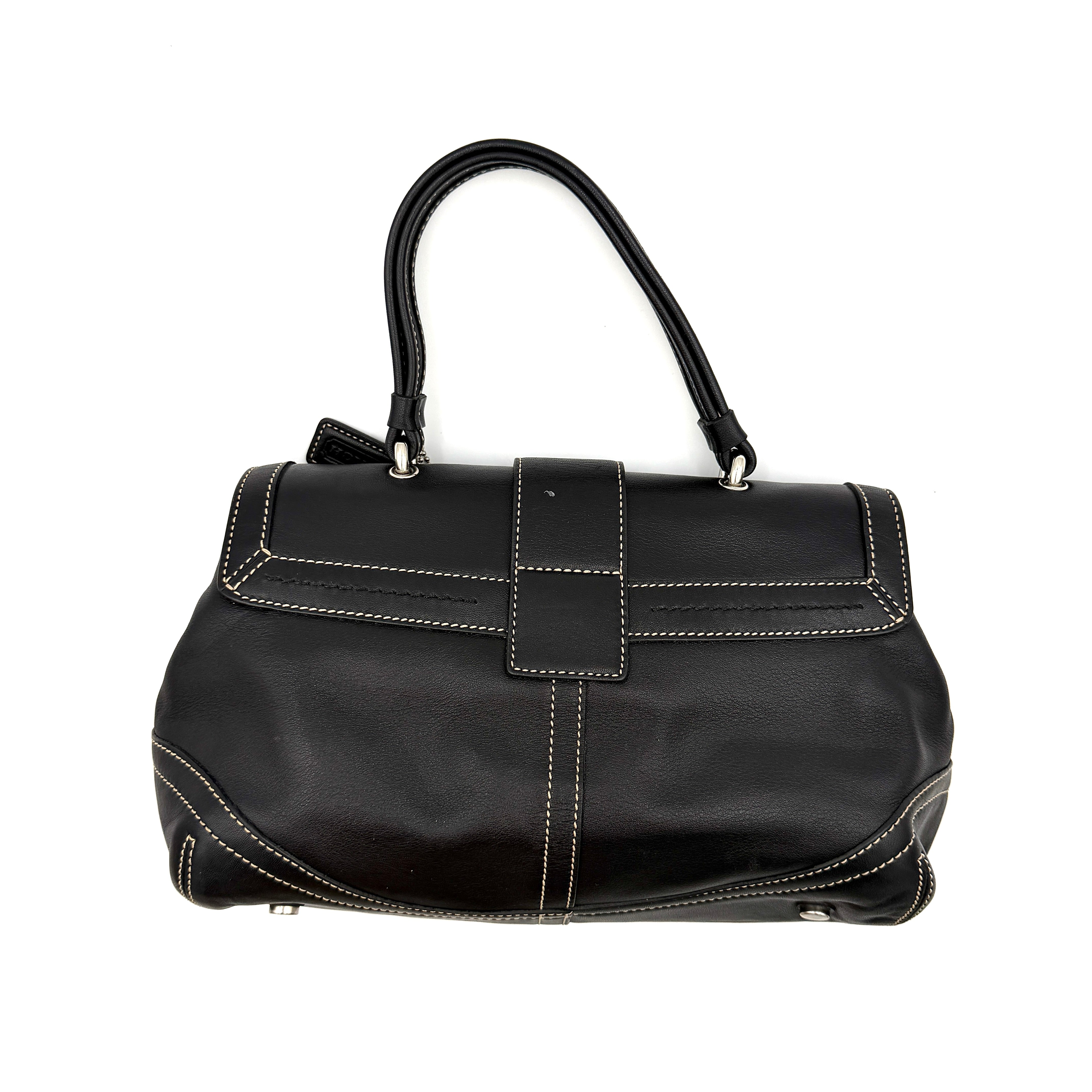 Coach Soho Buckle Top Handle Bag in black leather with contrast stitching and silver buckle, presented against a white background.