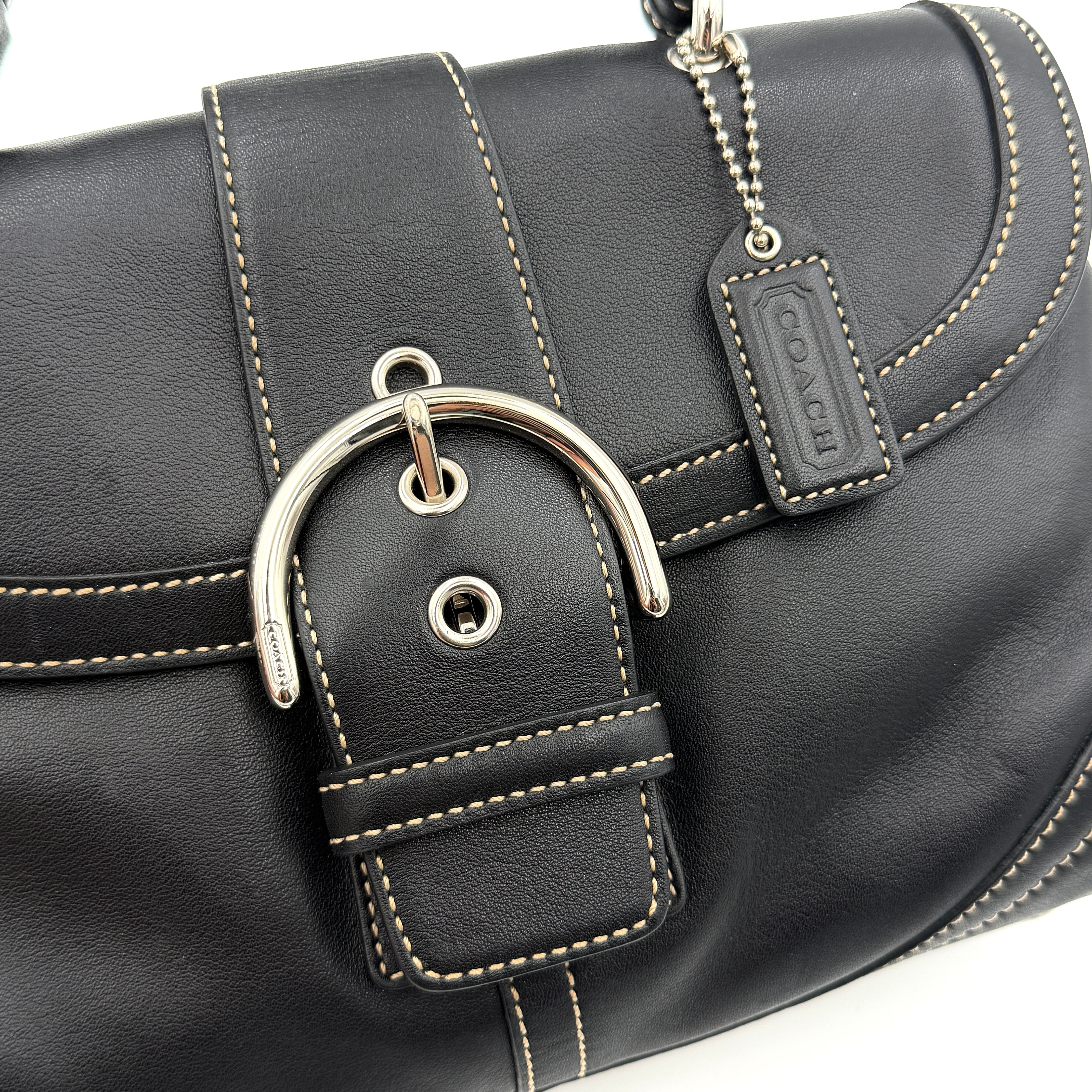 Coach Soho Buckle Top Handle Bag in black leather with contrast stitching and silver buckle, presented against a white background.