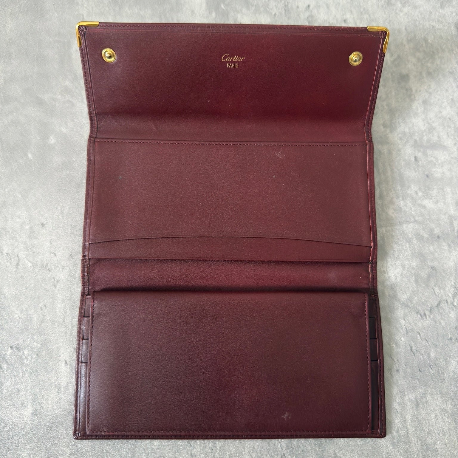 Cartier Must de Cartier trifold continental wallet in burgundy leather, showcasing detailed craftsmanship, gold-tone Cartier logo, and an organized interior.