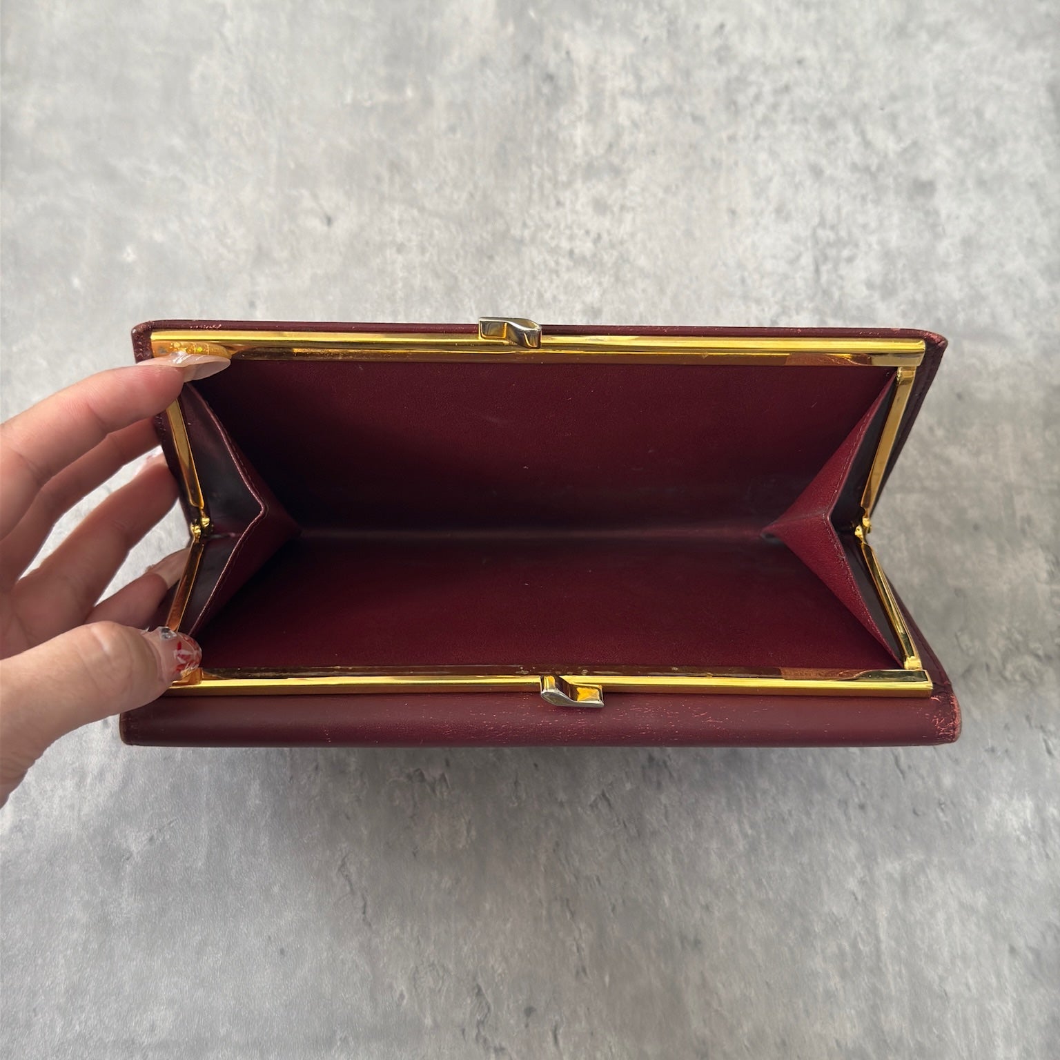 Cartier Must de Cartier trifold continental wallet in burgundy leather, showcasing detailed craftsmanship, gold-tone Cartier logo, and an organized interior.